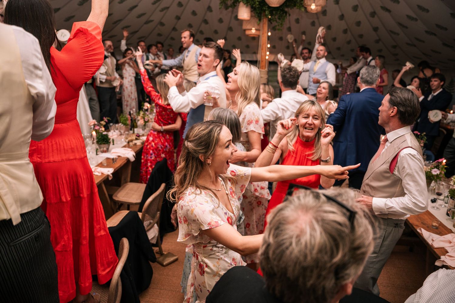 Energetic wedding guests dancing and celebrating in festive decorated marquee reception tent.