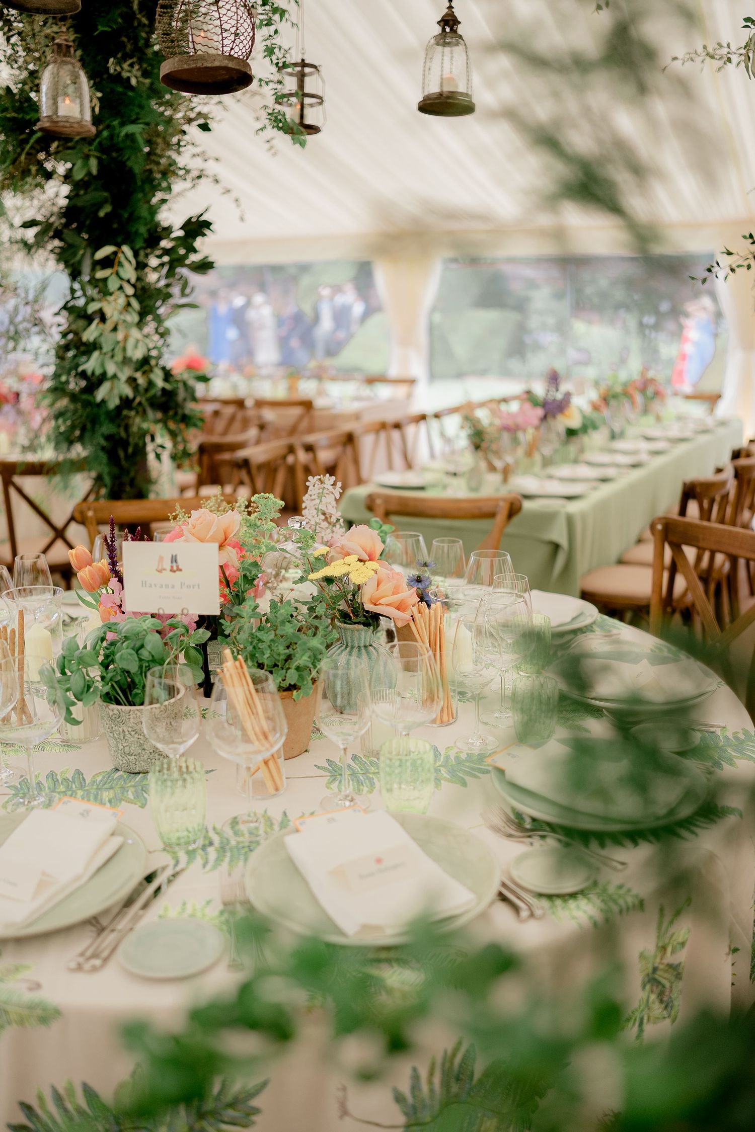 Elegant wedding reception marquee with floral centerpieces and green botanical table linens.