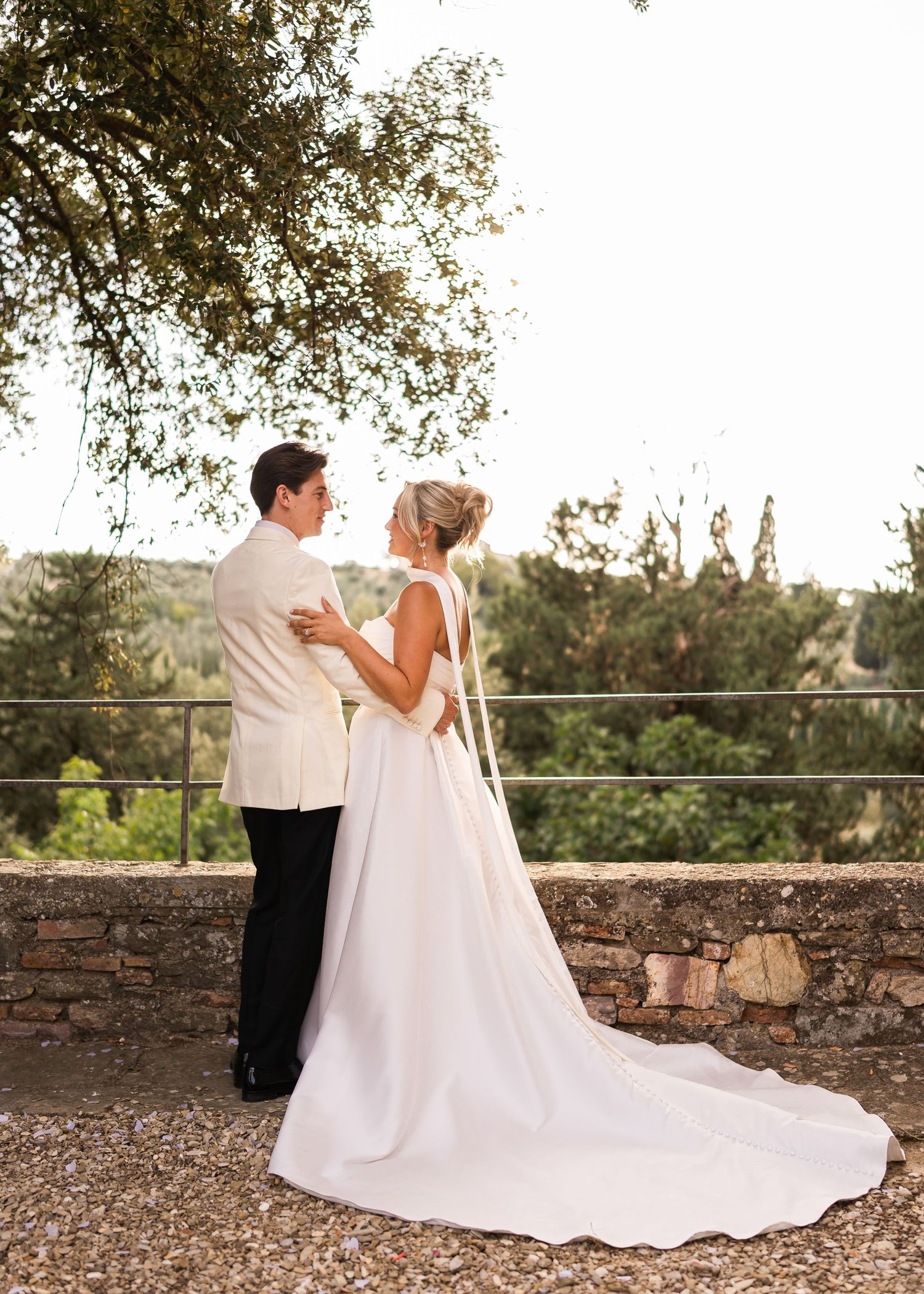 Bride and groom embracing on a stone terrace surrounded by lush greenery at their outdoor wedding.
