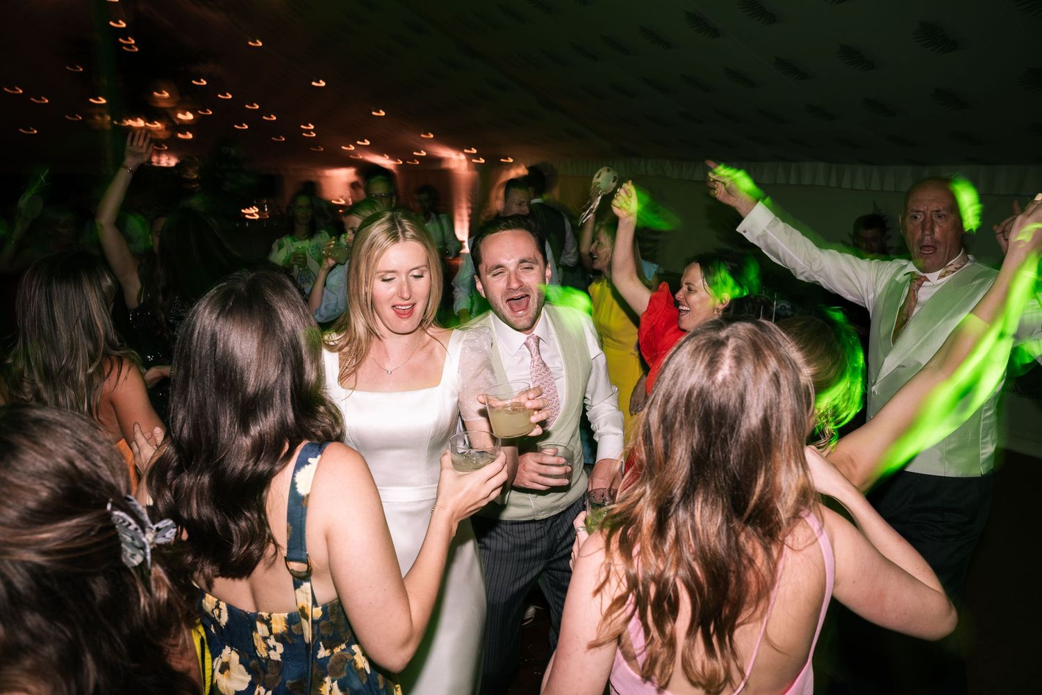 Bride and groom celebrating joyfully with guests on a wedding reception dance floor.