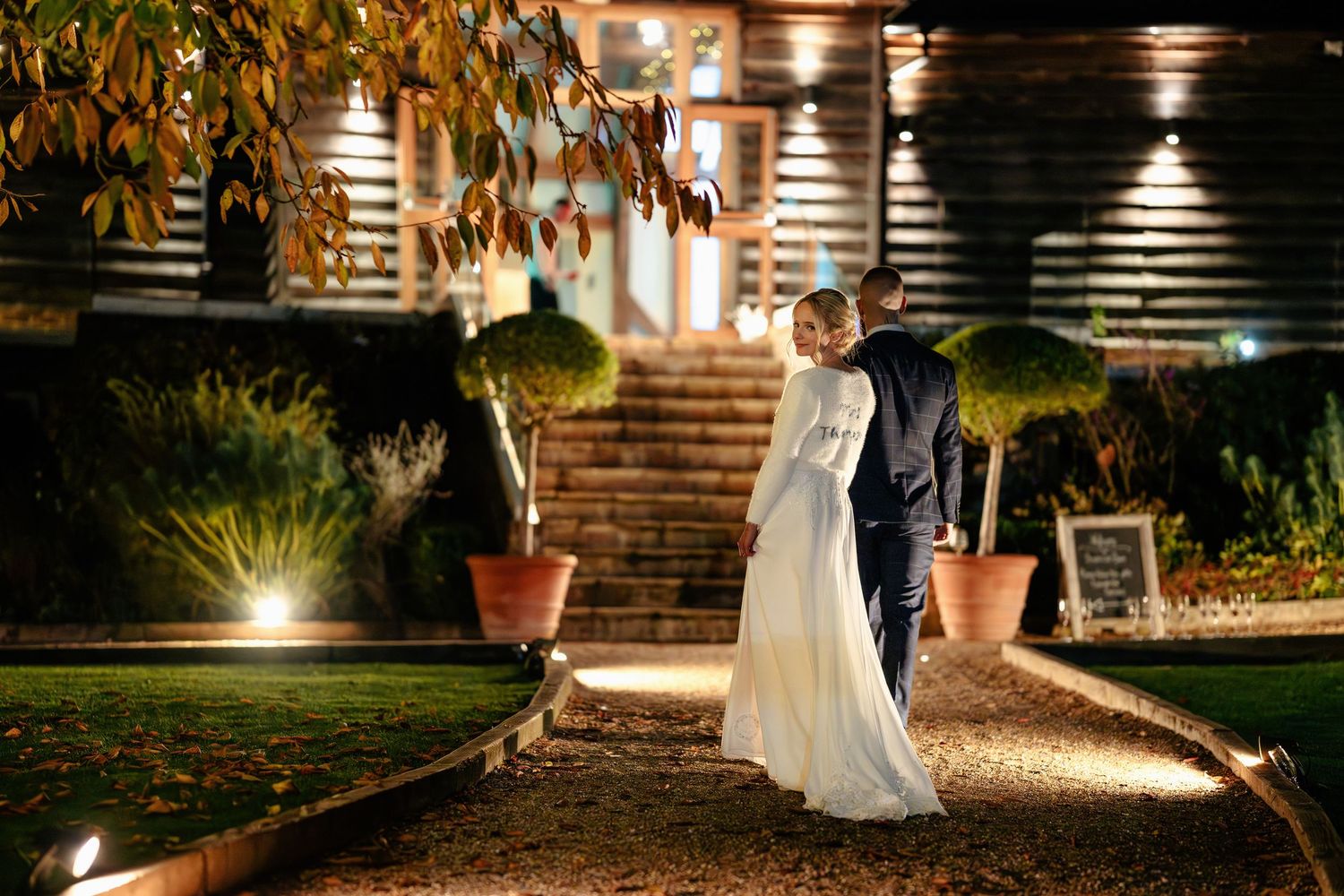 Bride and groom share romantic moment outside illuminated rustic wedding venue at night.