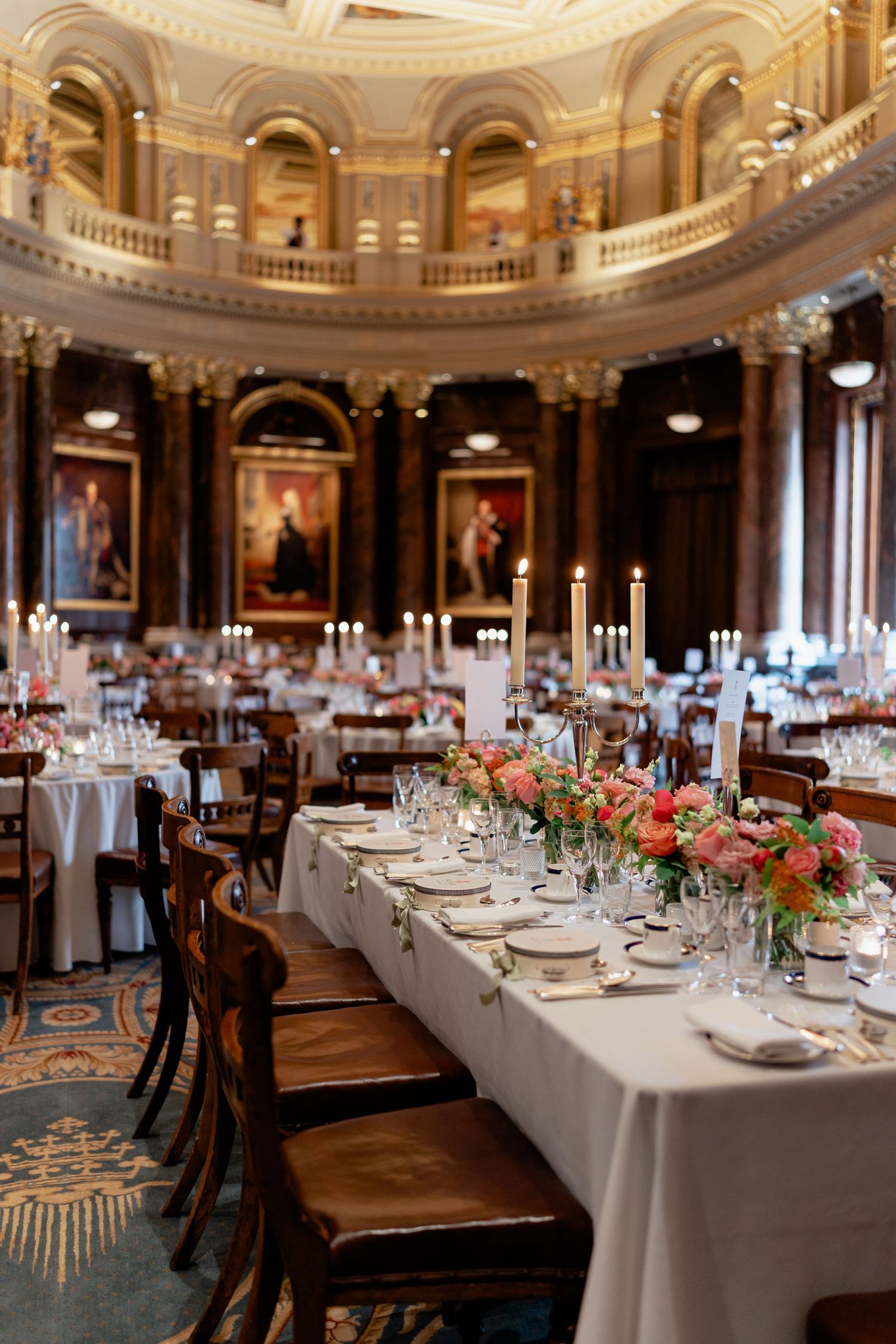 Elegant wedding reception in a grand hall with tall candles, pink floral centerpieces, and portraits.