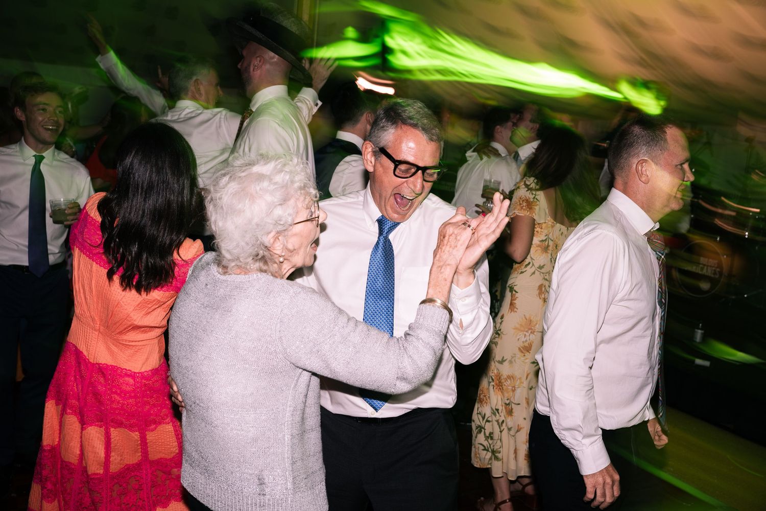 Elderly couple dancing together at a wedding reception under green party lights.
