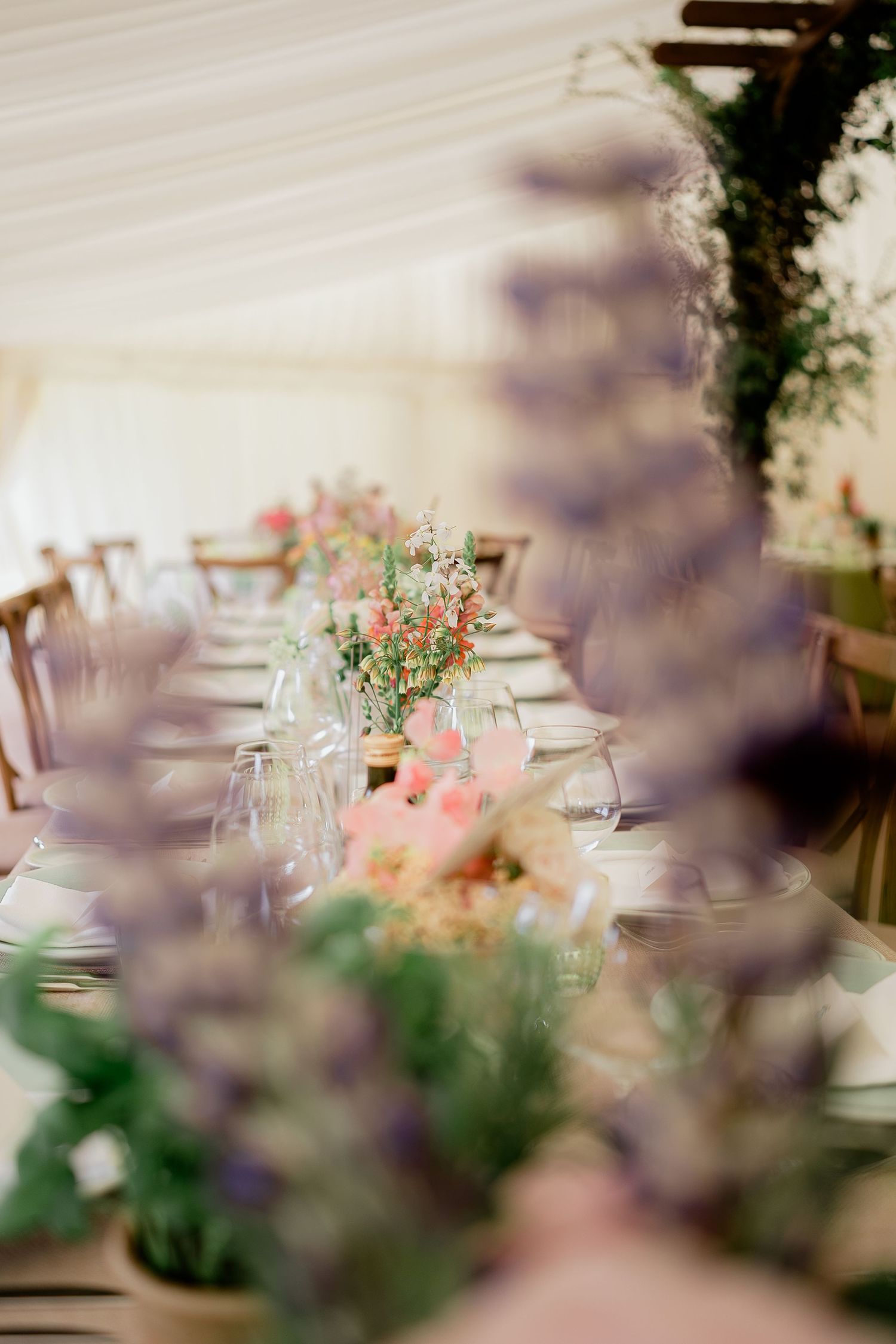 Dreamy wedding reception table setting with pastel floral arrangements inside a marquee tent.