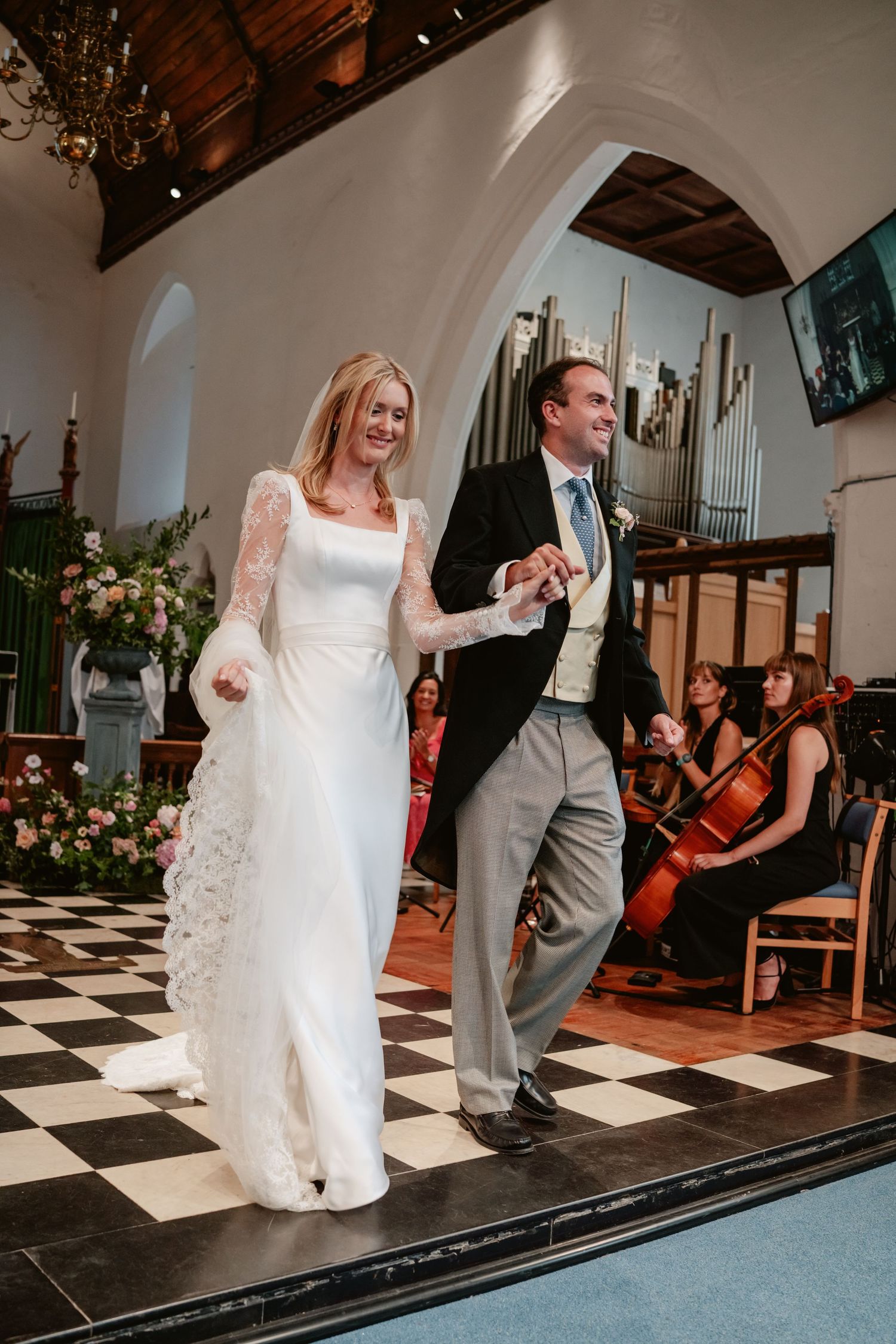 Joyful bride and groom walking down the aisle of a church with a checkered floor.