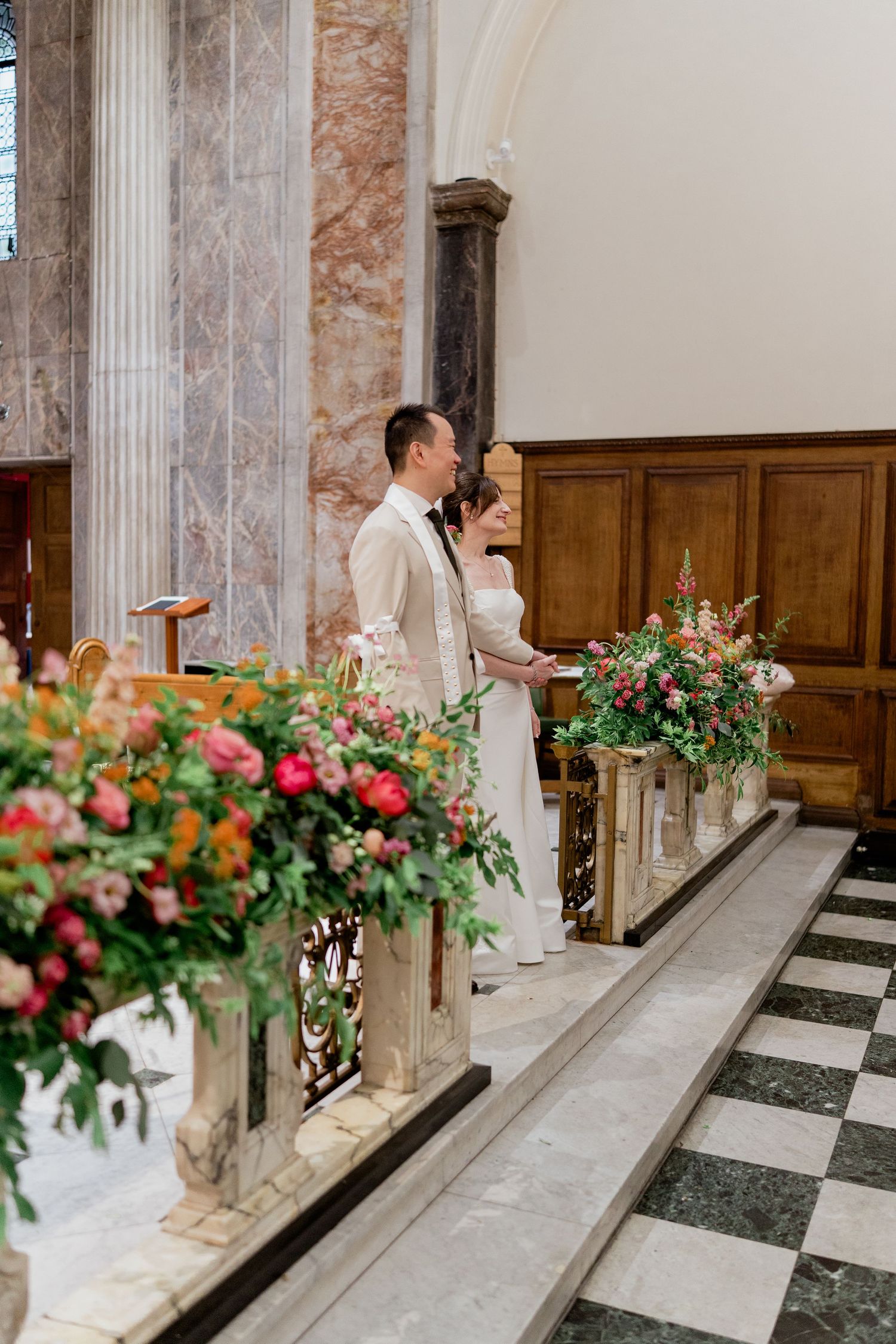 Bride and groom standing at the altar of an elegant church adorned with colorful floral arrangements.