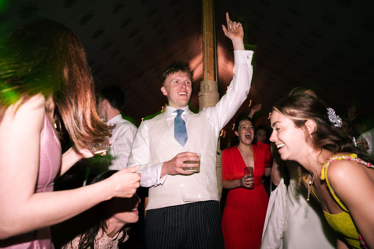 Excited man in white shirt dancing with hands raised at a lively wedding party.
