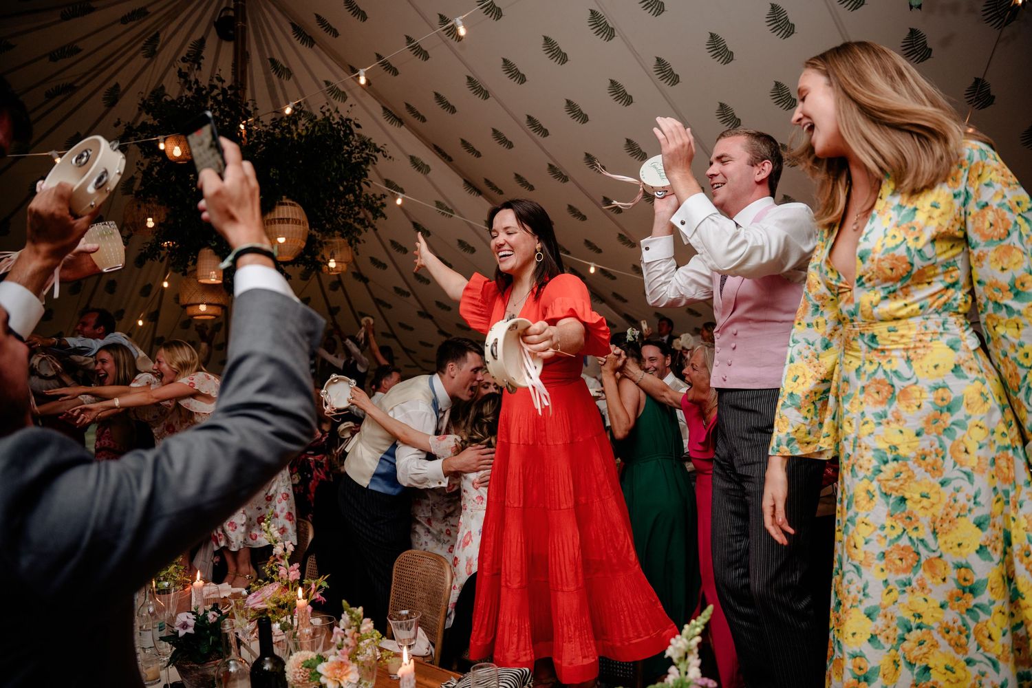 Guests dancing joyfully at a wedding reception inside a decorated tent with festive string lights.
