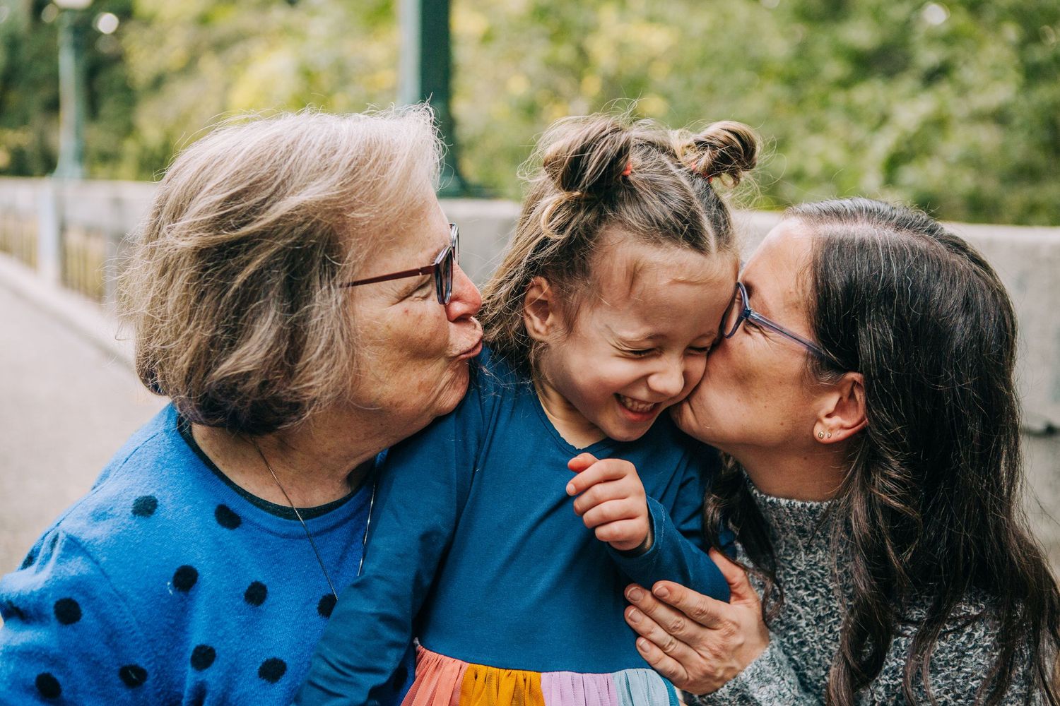 Grandmother and mother kissing young girl on cheeks outdoors, three-generation family sharing a joyful moment. in Seattle WA at WA Arboretum