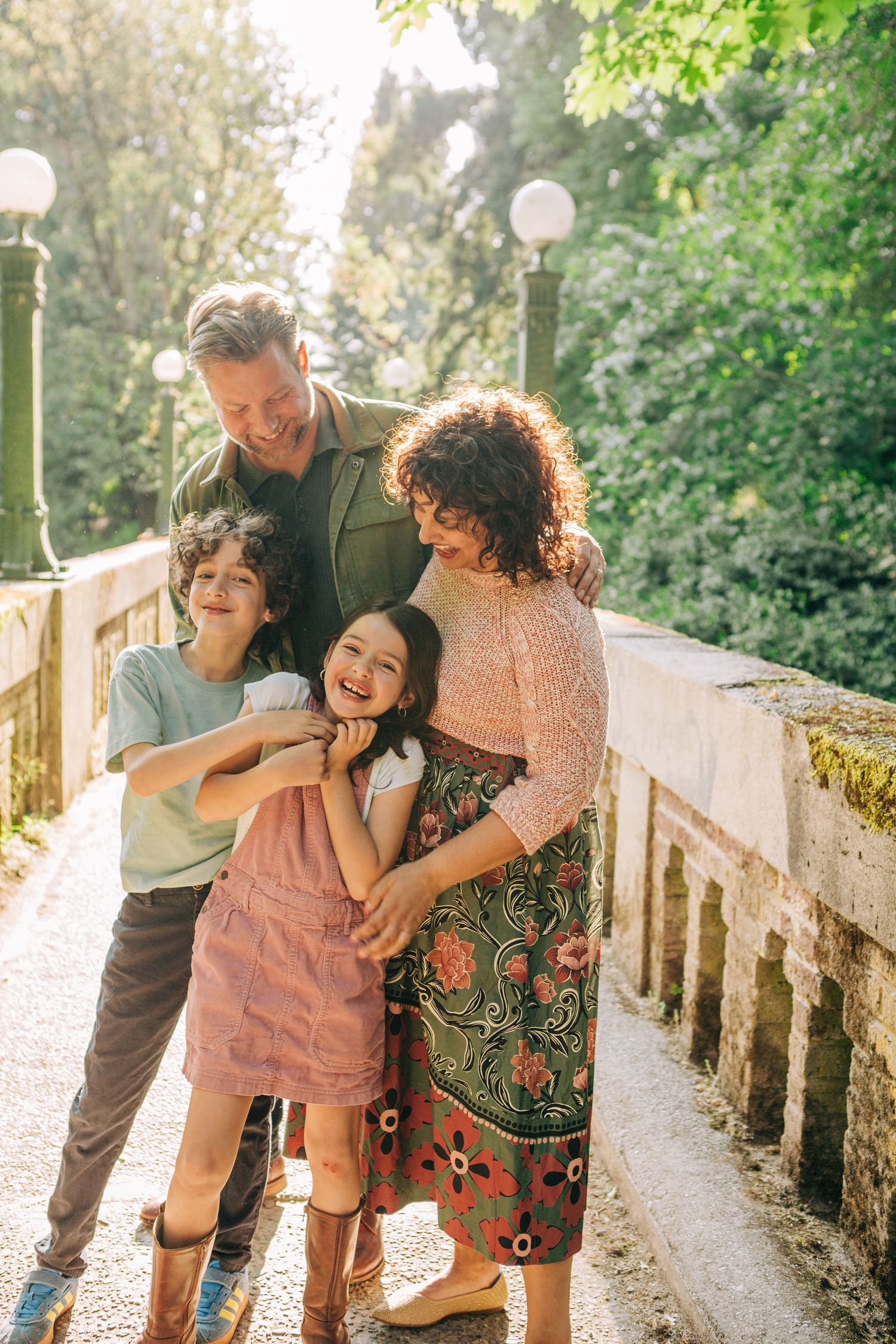 In Seattle, Washington at the WA Arboretum // Happy family of four laughing together on a sunlit park bridge surrounded by lush green trees.