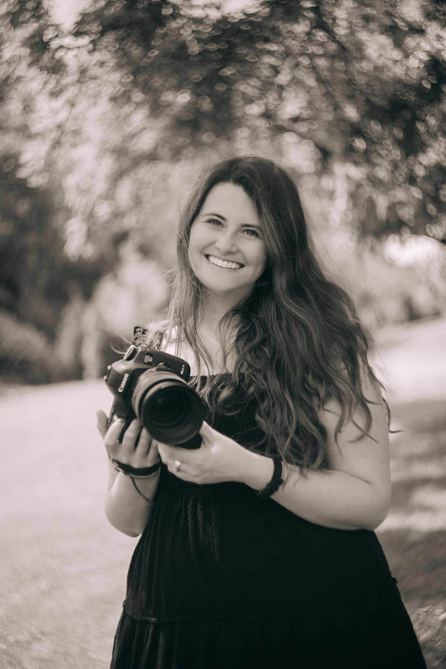 Smiling woman with long hair holding a DSLR camera outdoors in a sepia-toned portrait photo. in Seattle Washington Lexi Laginess Photography