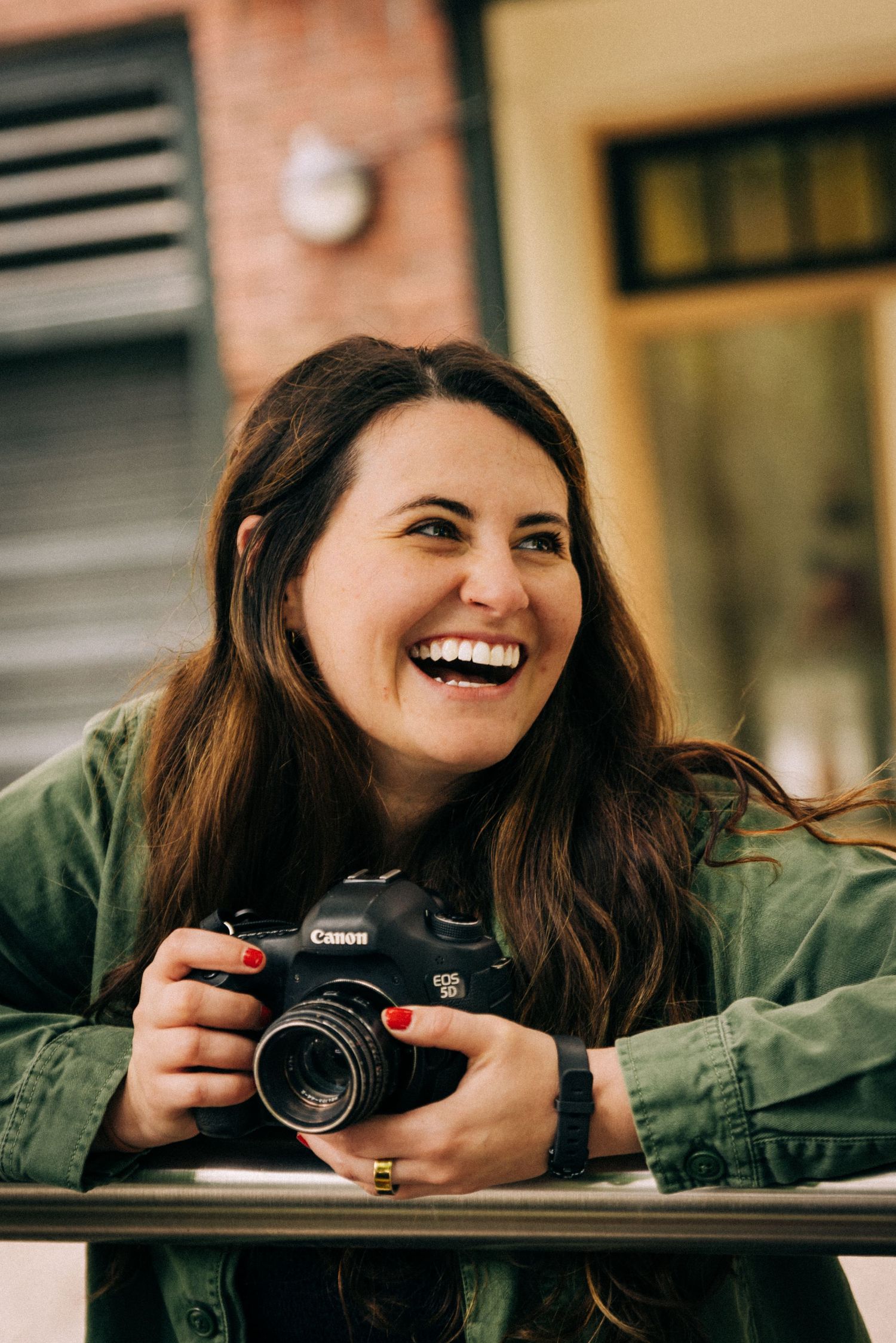 in Seattle WA. A smiling woman holding a Canon EOS DSLR camera outdoors, wearing a green jacket. Downtown Seattle Family  Photographer