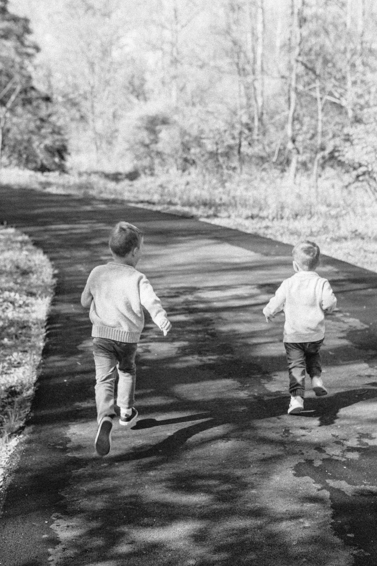 Two young boys running together down a paved park path surrounded by trees in a black and white photo. in Seattle Washington