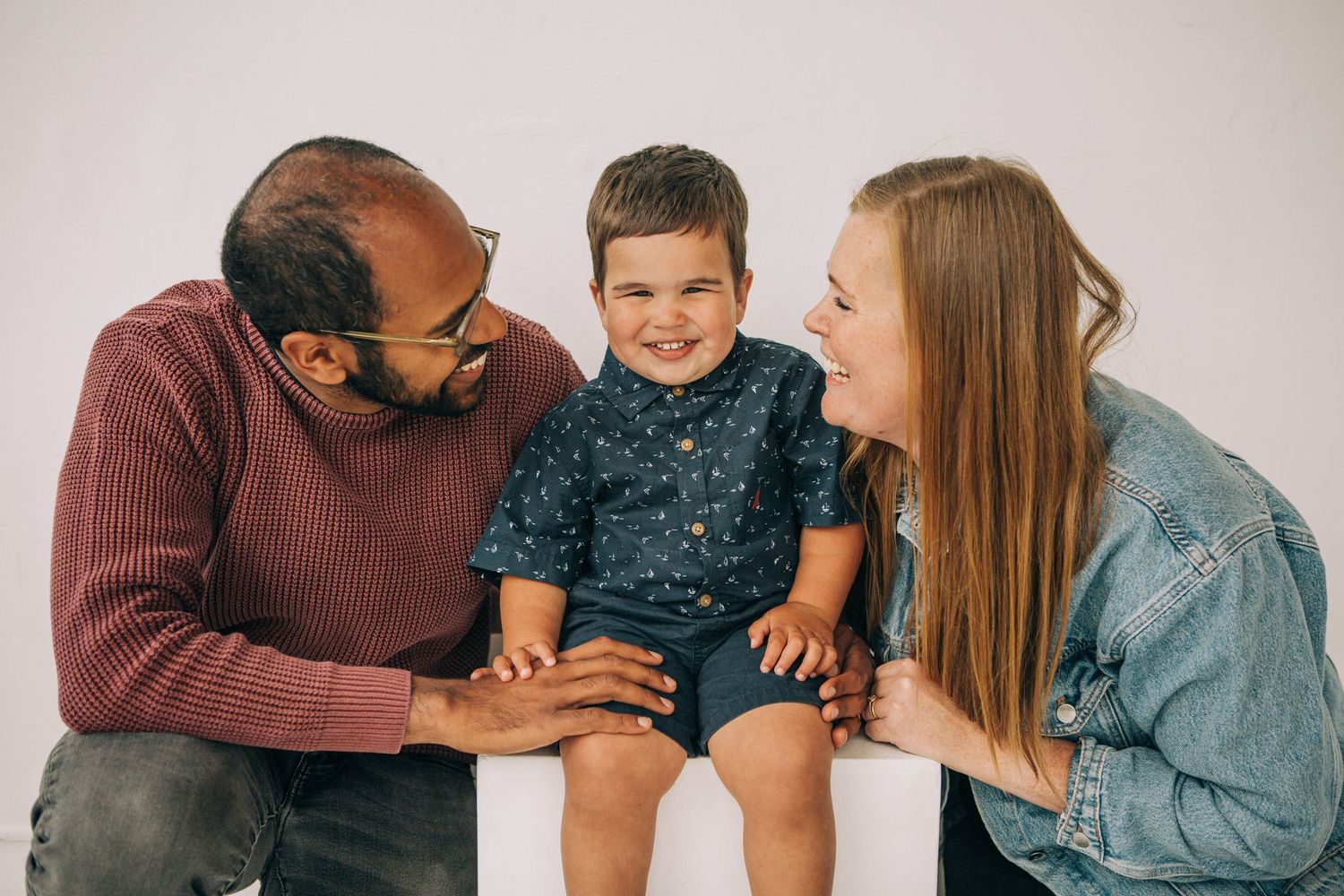 Happy family portrait with parents smiling at their toddler son sitting between them on white background. in Seattle Washington at Studio