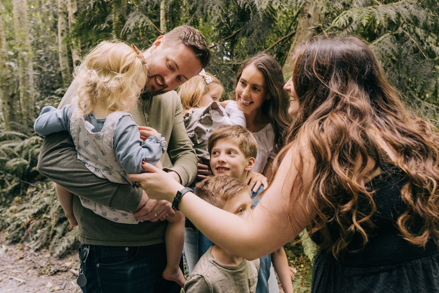 IN SEATTLE WA A joyful family with young children laughing and embracing outdoors in a lush green forest setting. for photographer