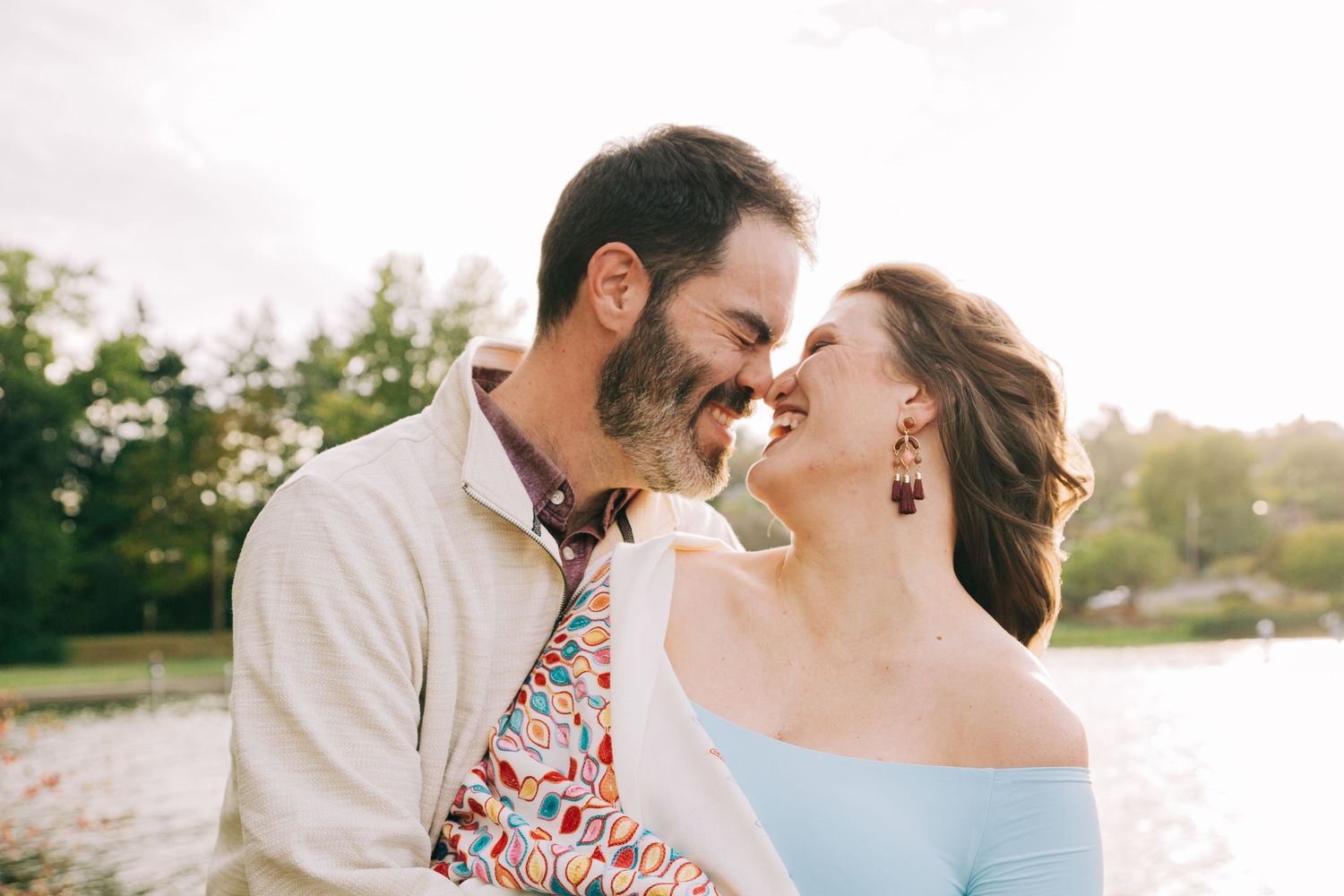 Joyful couple laughing and smiling closely together near a sunlit lake Washington in Seward Park, Seattle, Washington