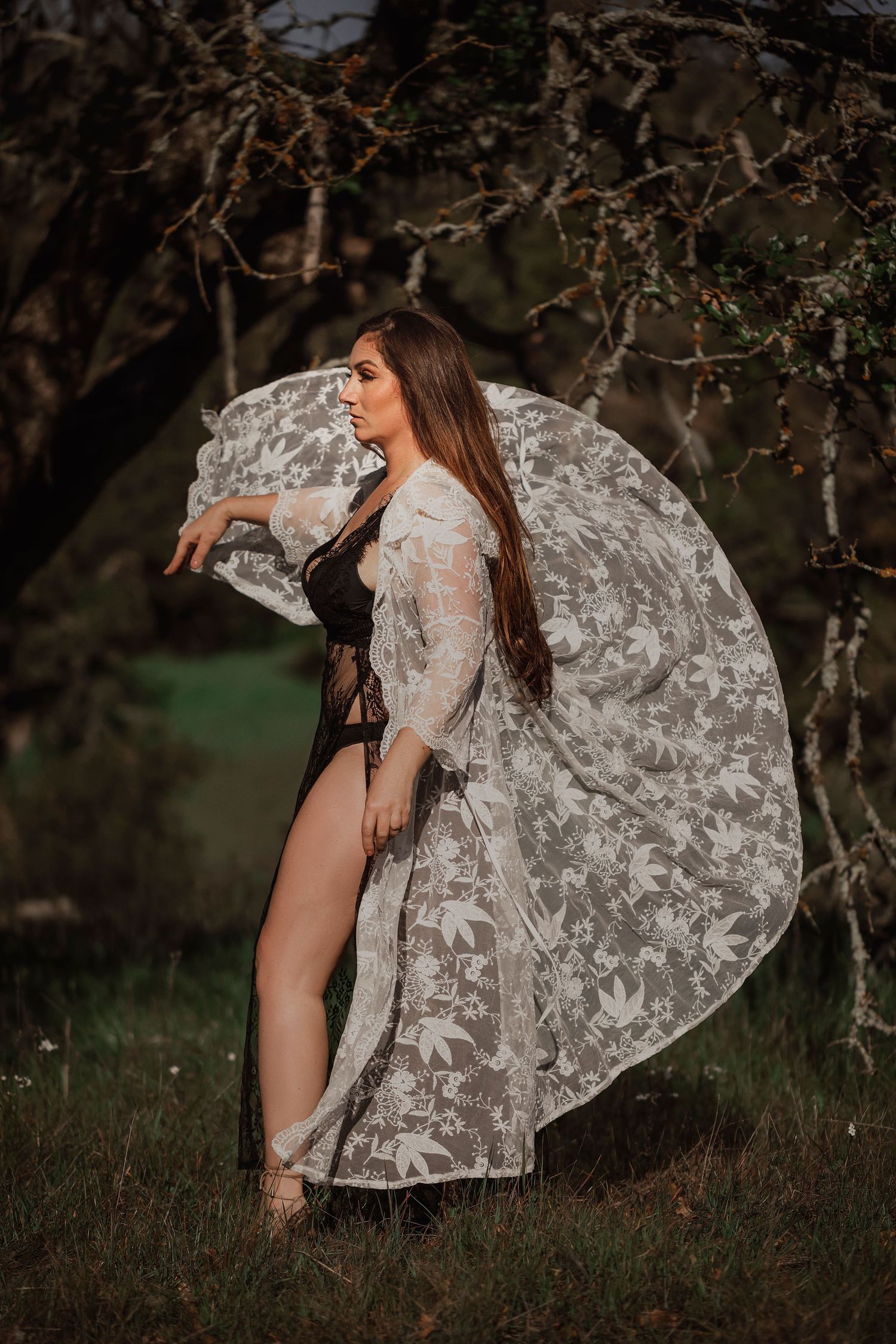 Find art portrait of a woman in a flowing lace dress photographed outdoors among natural woodland textures