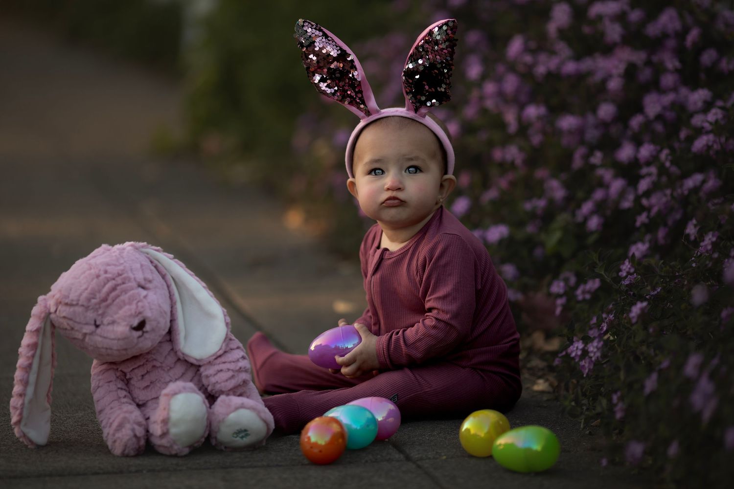 Fine art child portrait featuring a baby in bunny ears surrounded by spring flowers and Easter eggs