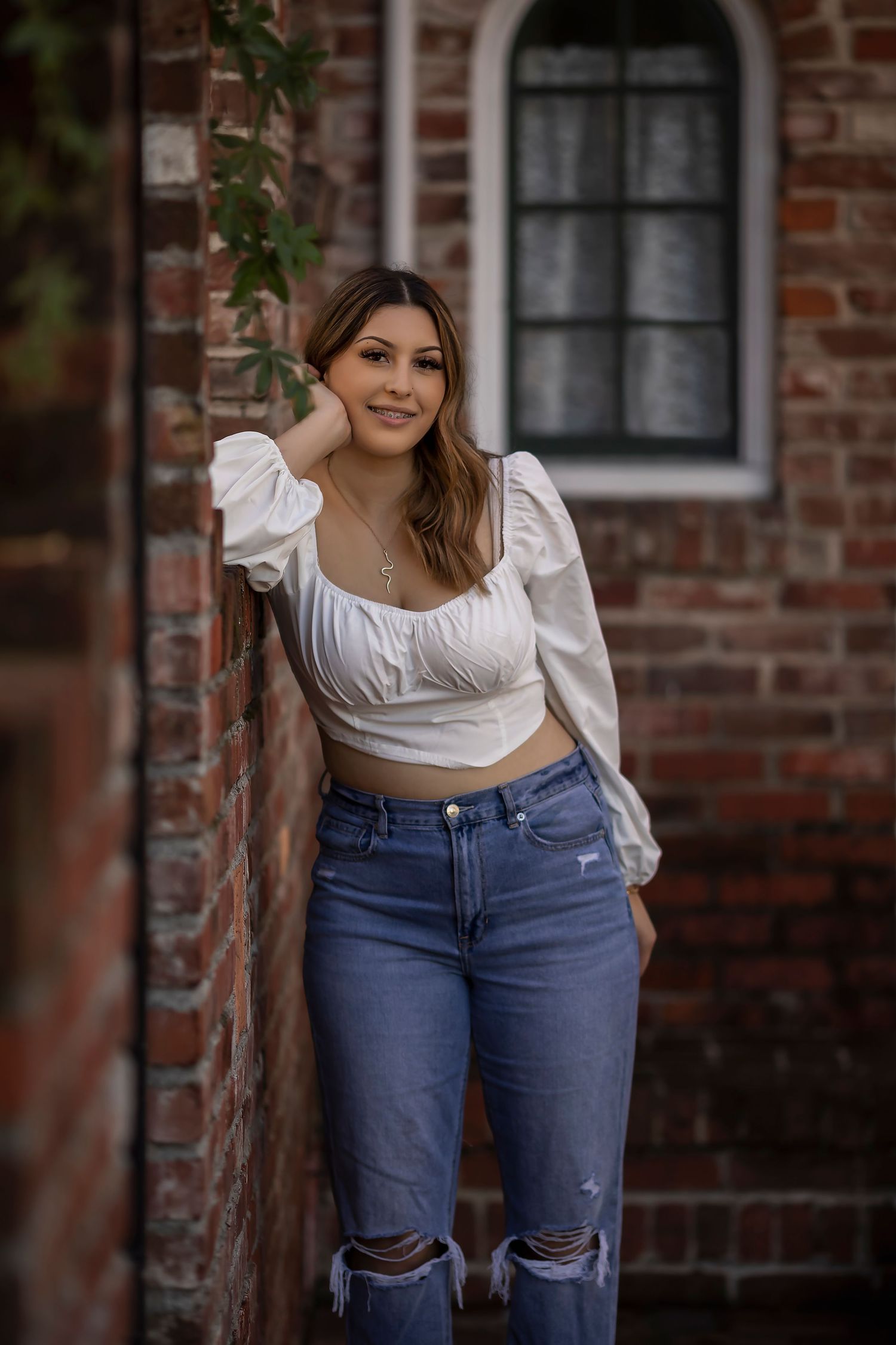 Outdoor senior portrait of a young woman posed against historic brick architecture and garden surroundings