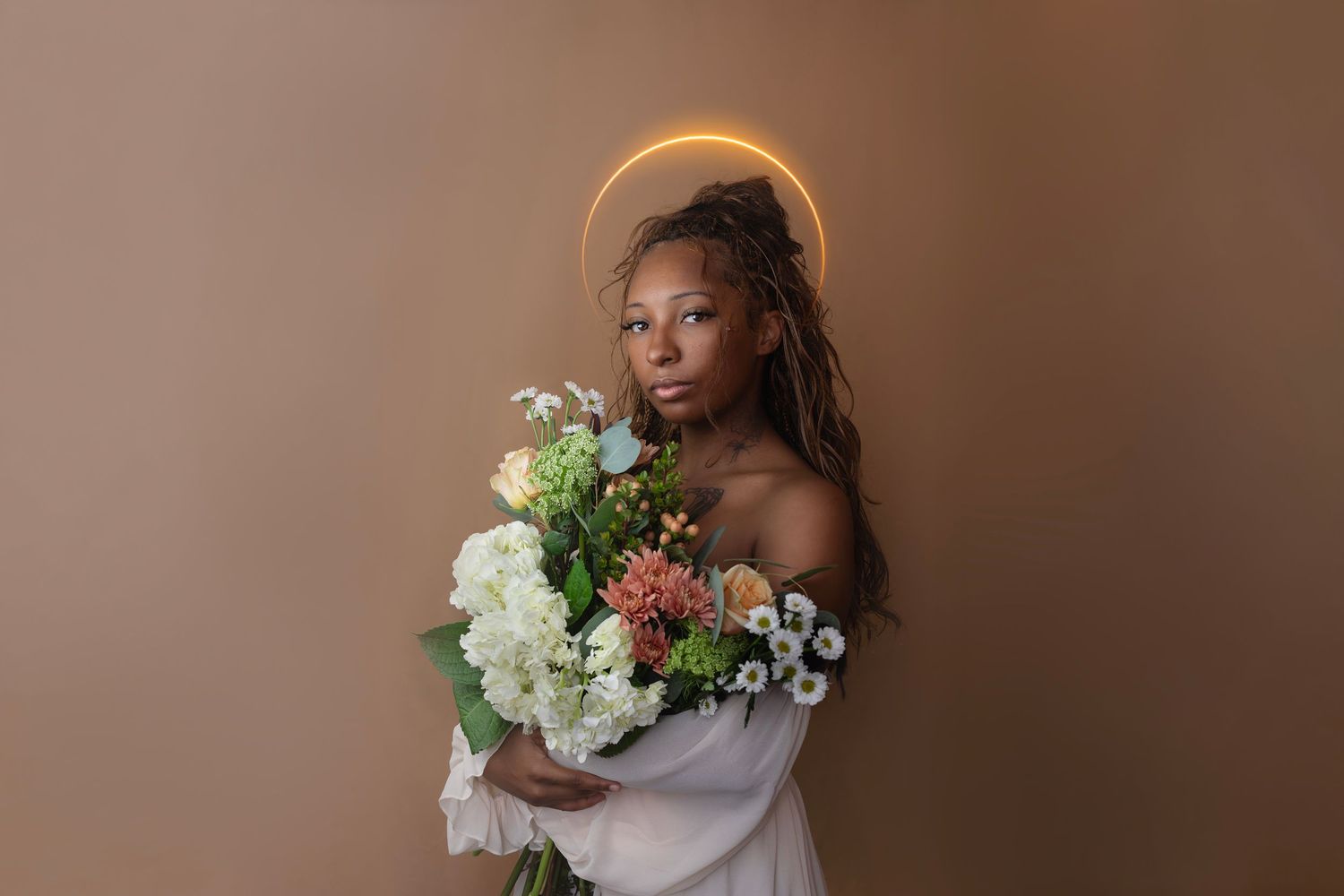 Fine art portrait of woman holding flowers with a glowing halo during a creative in-home portrait session.