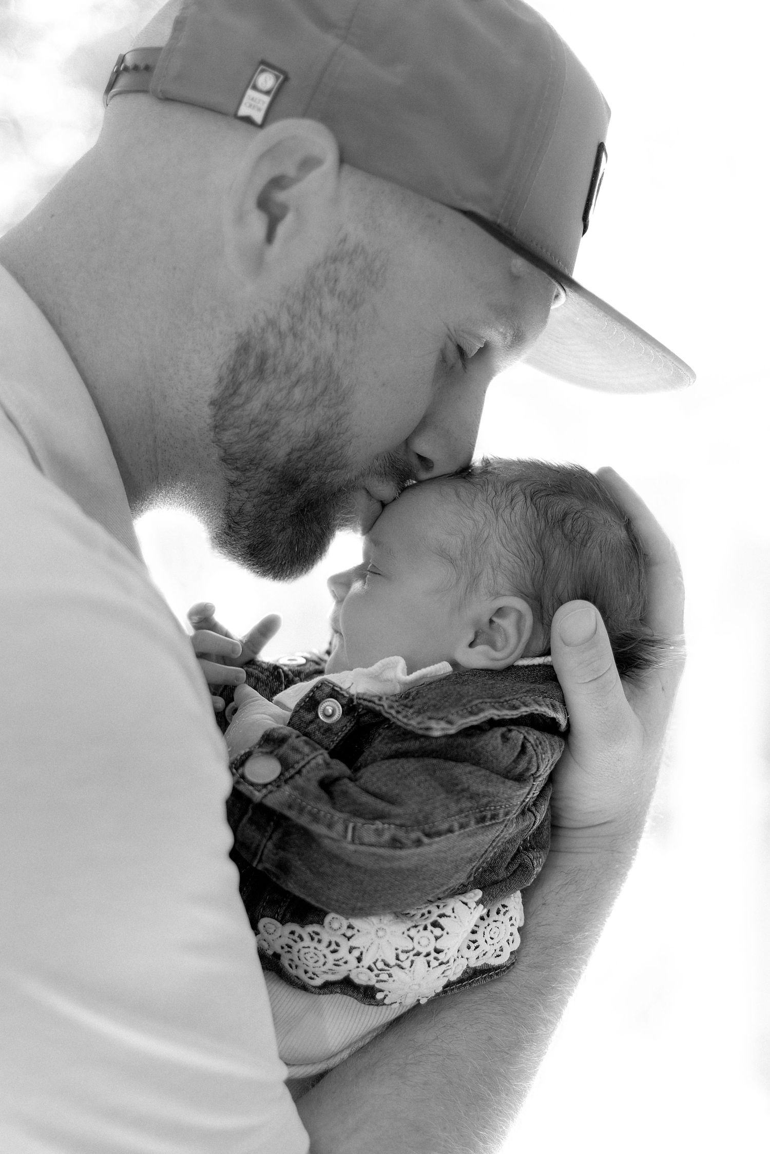 Black-and-white newborn lifestyle portrait capturing a father holding and kissing his baby