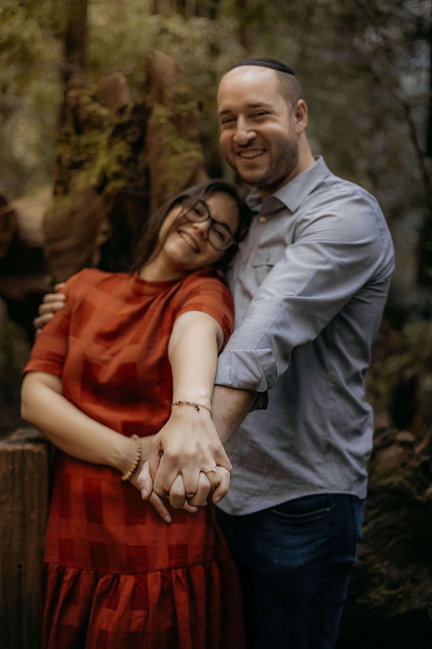 Romantic engagement portrait featuring a couple embracing outdoors in natural woodland surroundings