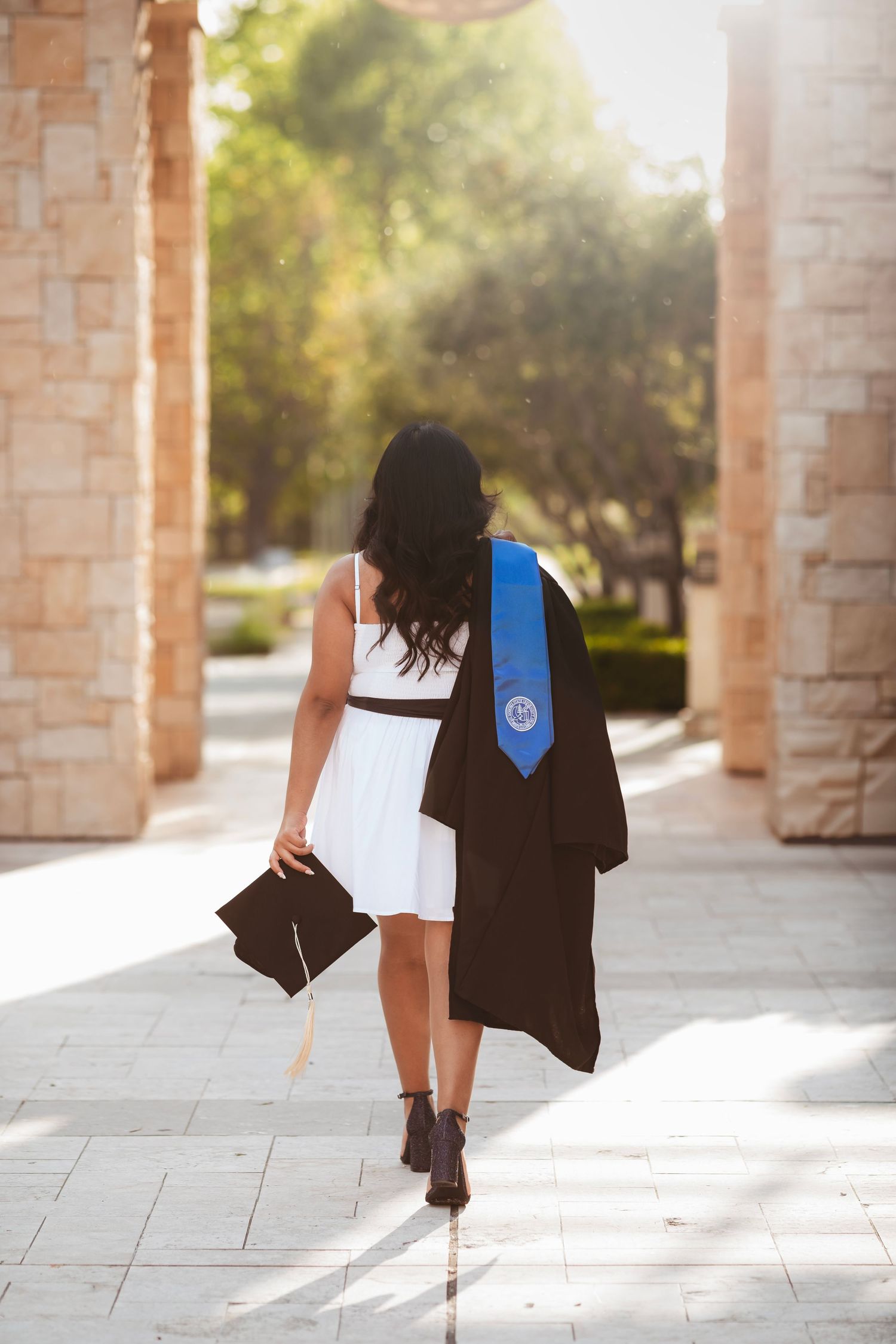 Graduation portrait of a young woman and a cap and gown walking through a university campus at sunset