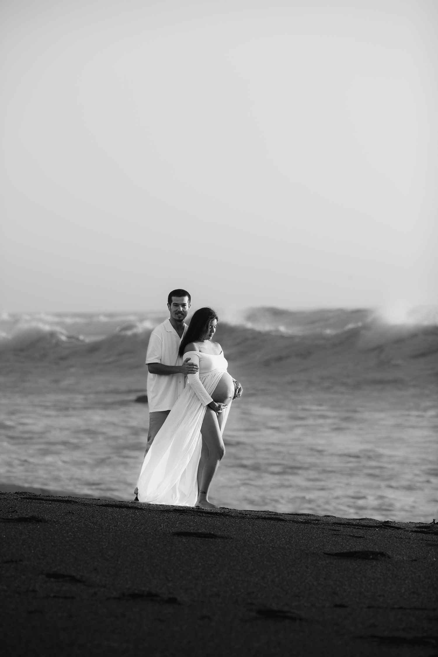 Black and white portrait of a couple embracing on a windswept beach during a romantic coastal photography session in Sonoma County.