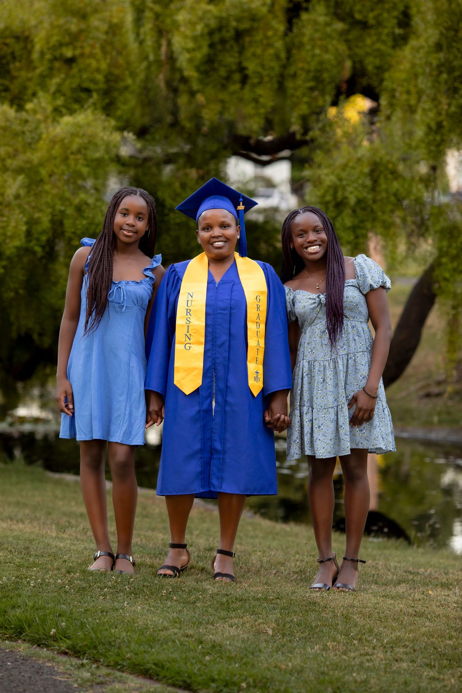 Graduation portrait session featuring a graduate in a blue cabin and gown celebrating with her daughters outdoors