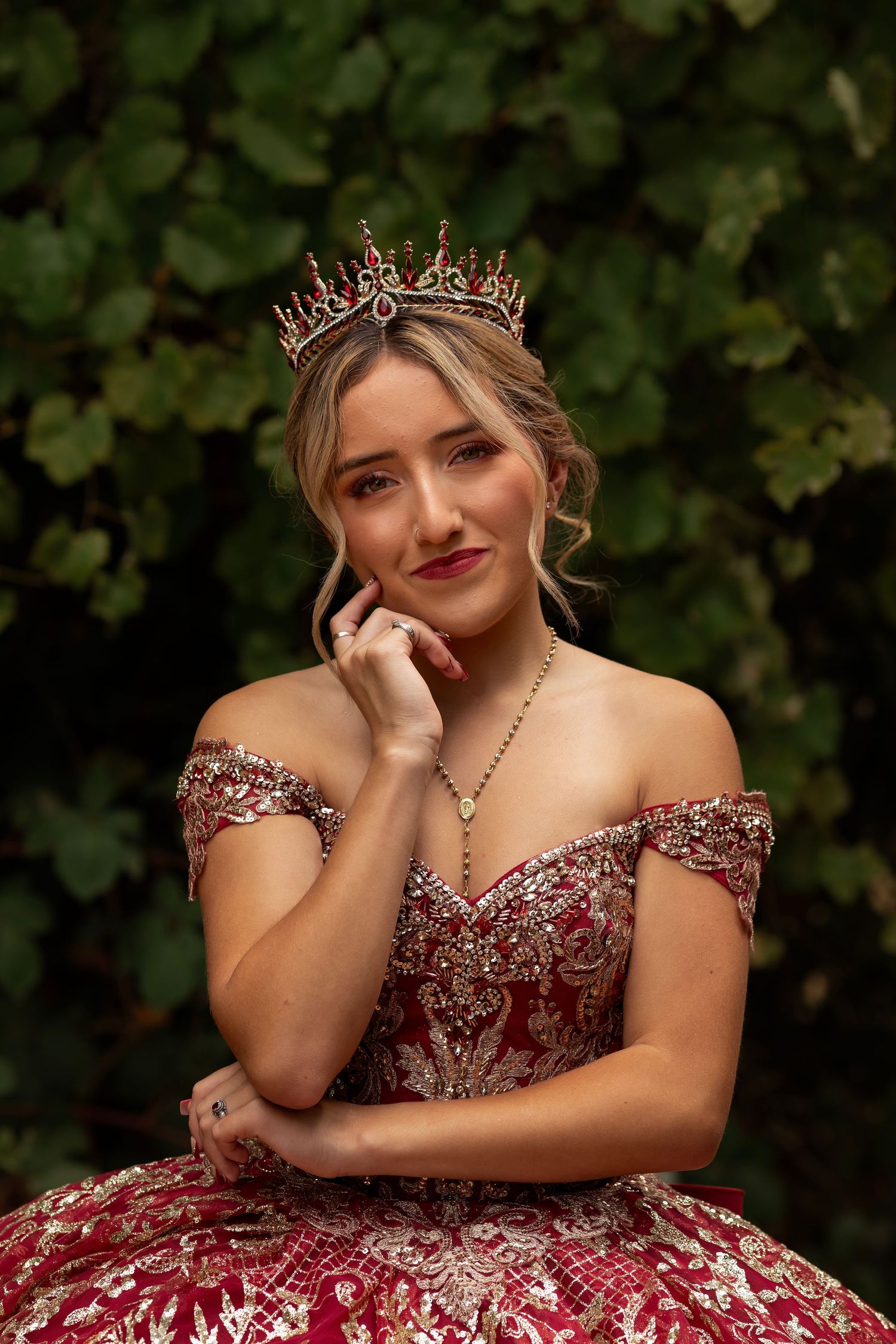 Elegant quinceañera portrait of a young woman wearing a crown and embroidered gown against a natural backdrop