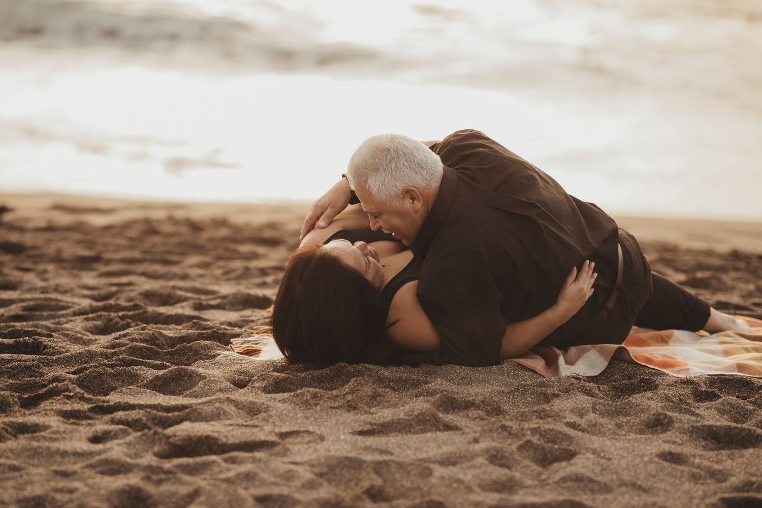 Long-married couple laughing and embracing on a beach during a romantic sunset portrait session on the Sonoma Coast.