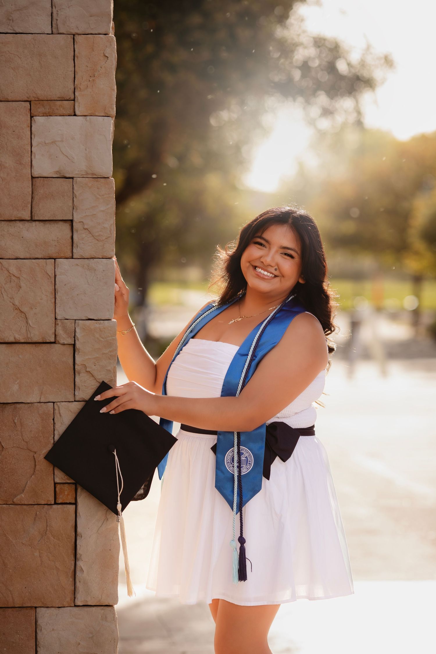 College graduation portrait featuring a young woman holding her cap in golden evening light