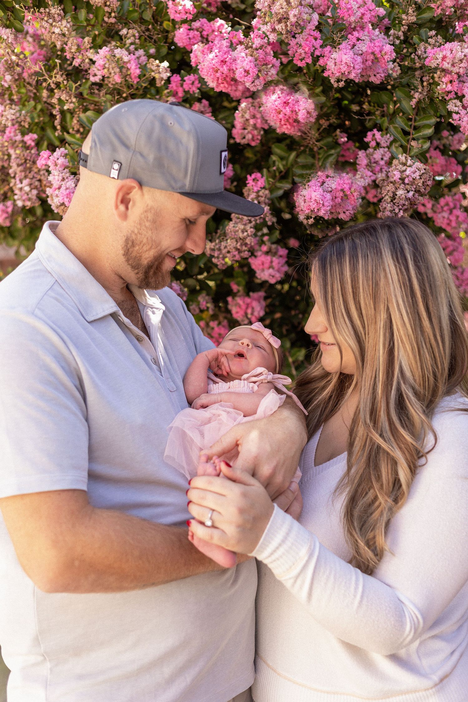 Family portrait featuring parents and their newborn baby photographed among blooming pink flowers