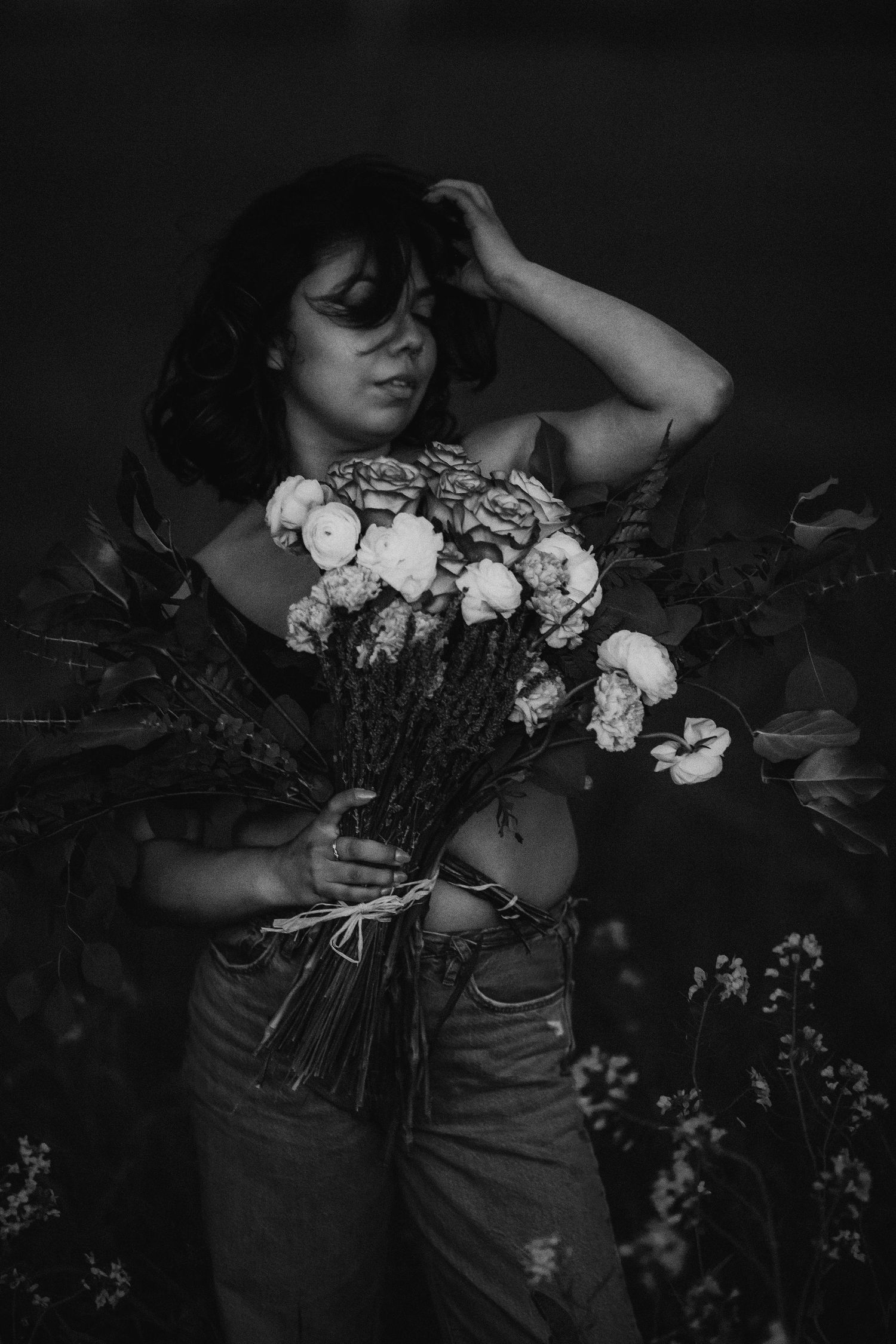 Black and white fine art portrait of a woman holding a bouquet of flowers against a dramatic dark background