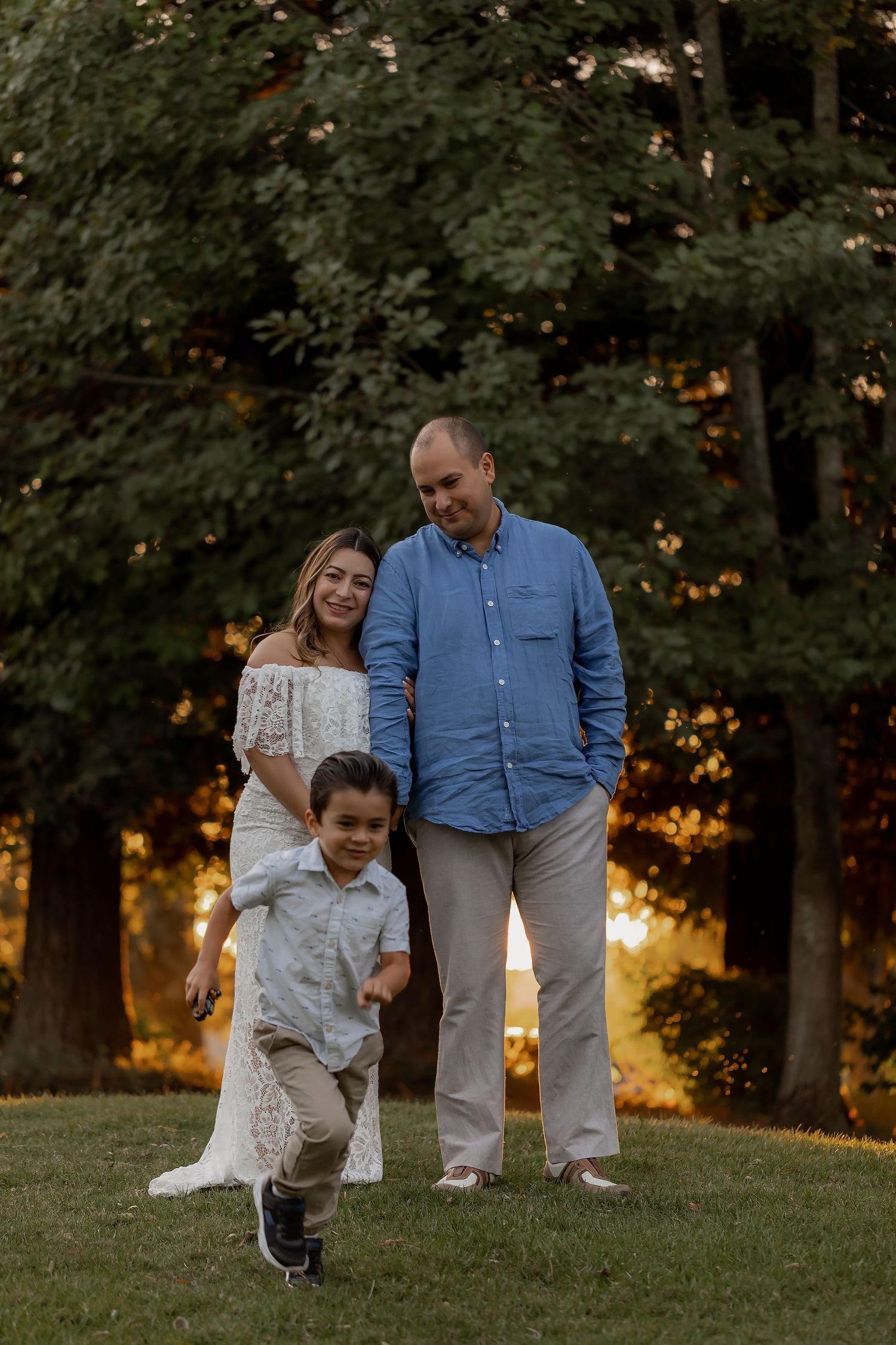 Family maternity portrait session featuring parents and young child photographed outdoors in natural evening life