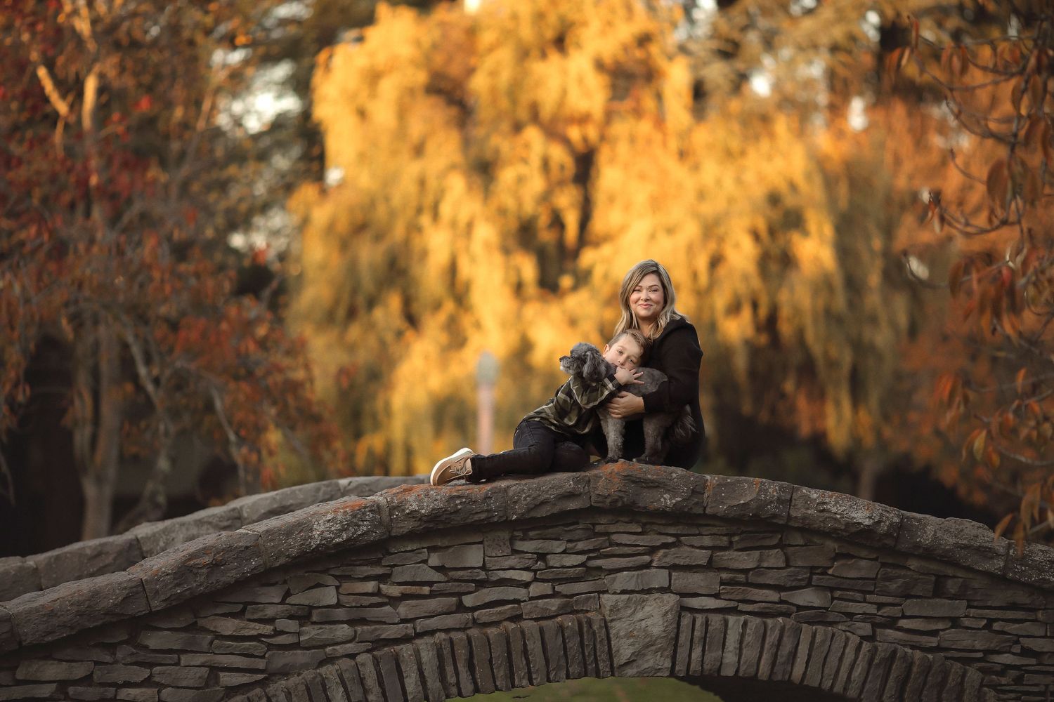 Fine art portrait of a woman seated on a historic stone bridge surrounded by vibrant autumn foliage in Sonoma county