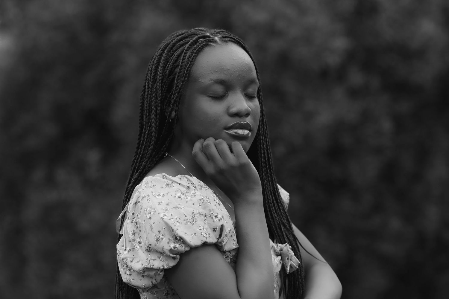 Black-and-white fine art portrait of a young woman with braided hair posed against a softly blurred background