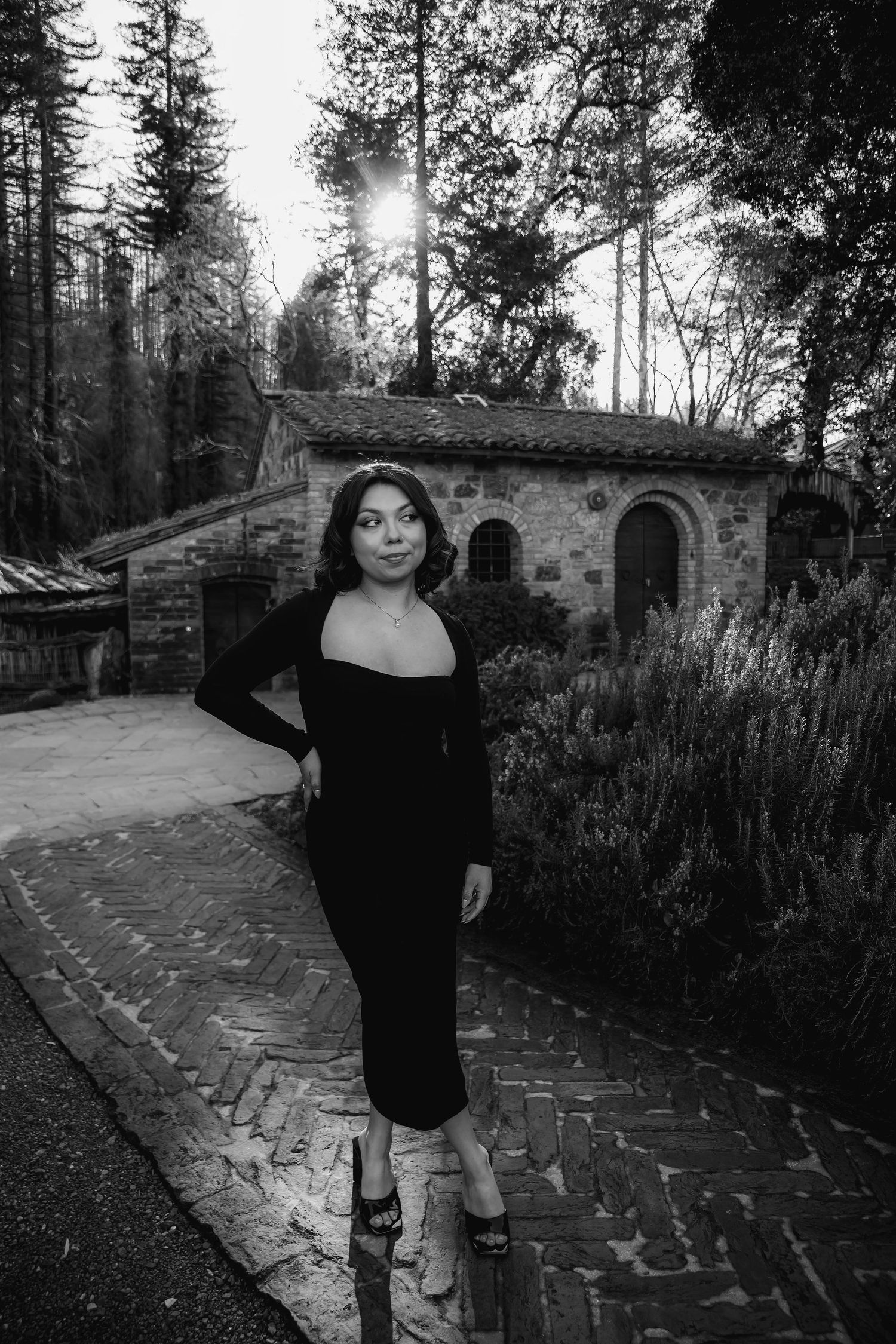 Black and white fine art portrait of a young woman walking along a garden pathway near a stone building