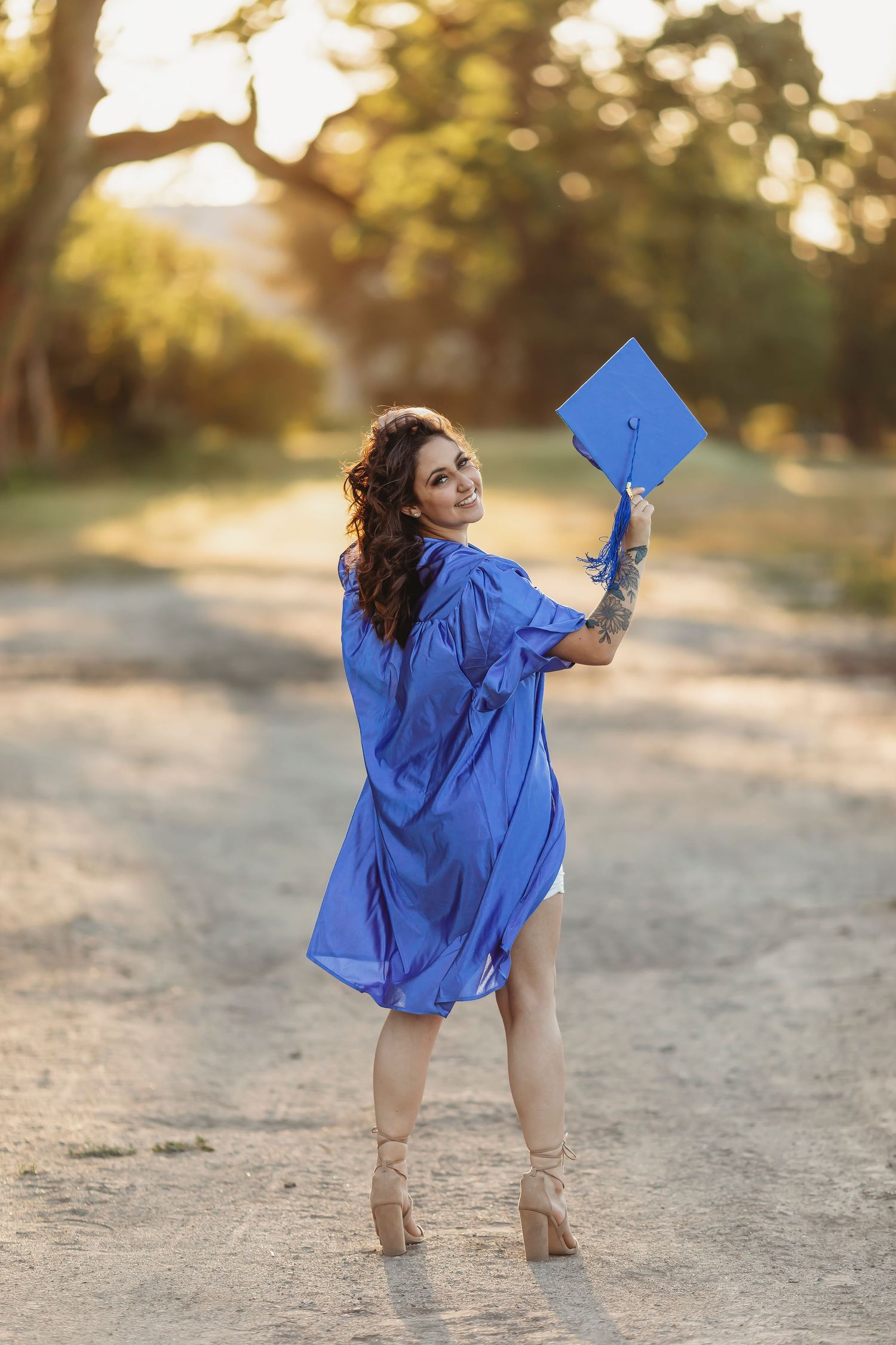 Fine art graduation portrait of a young woman in a blue cap & gown photographed outdoors in golden light