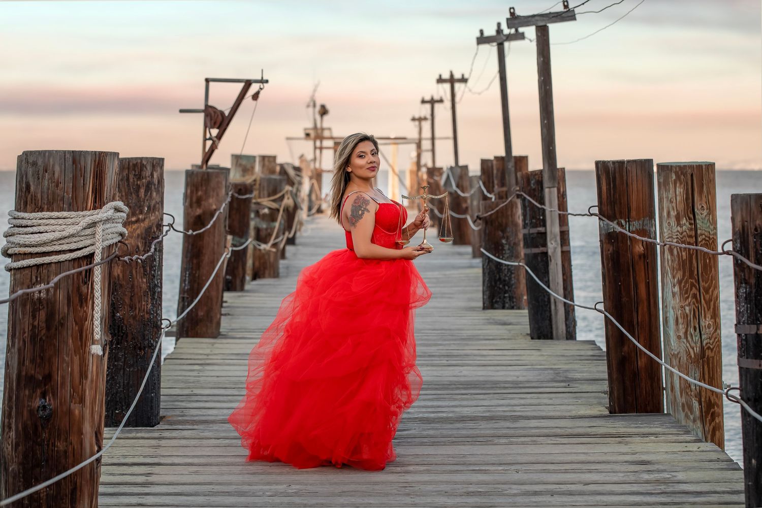 Fine art portrait of a woman in a flowing red gown photographed on a seaside pier at sunset