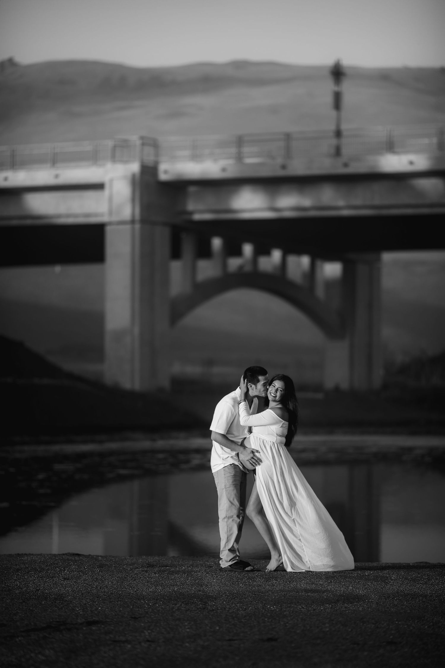 Black and white portrait of a couple standing beneath the pier during a fine art maternity photography session on the Sonoma Coast.