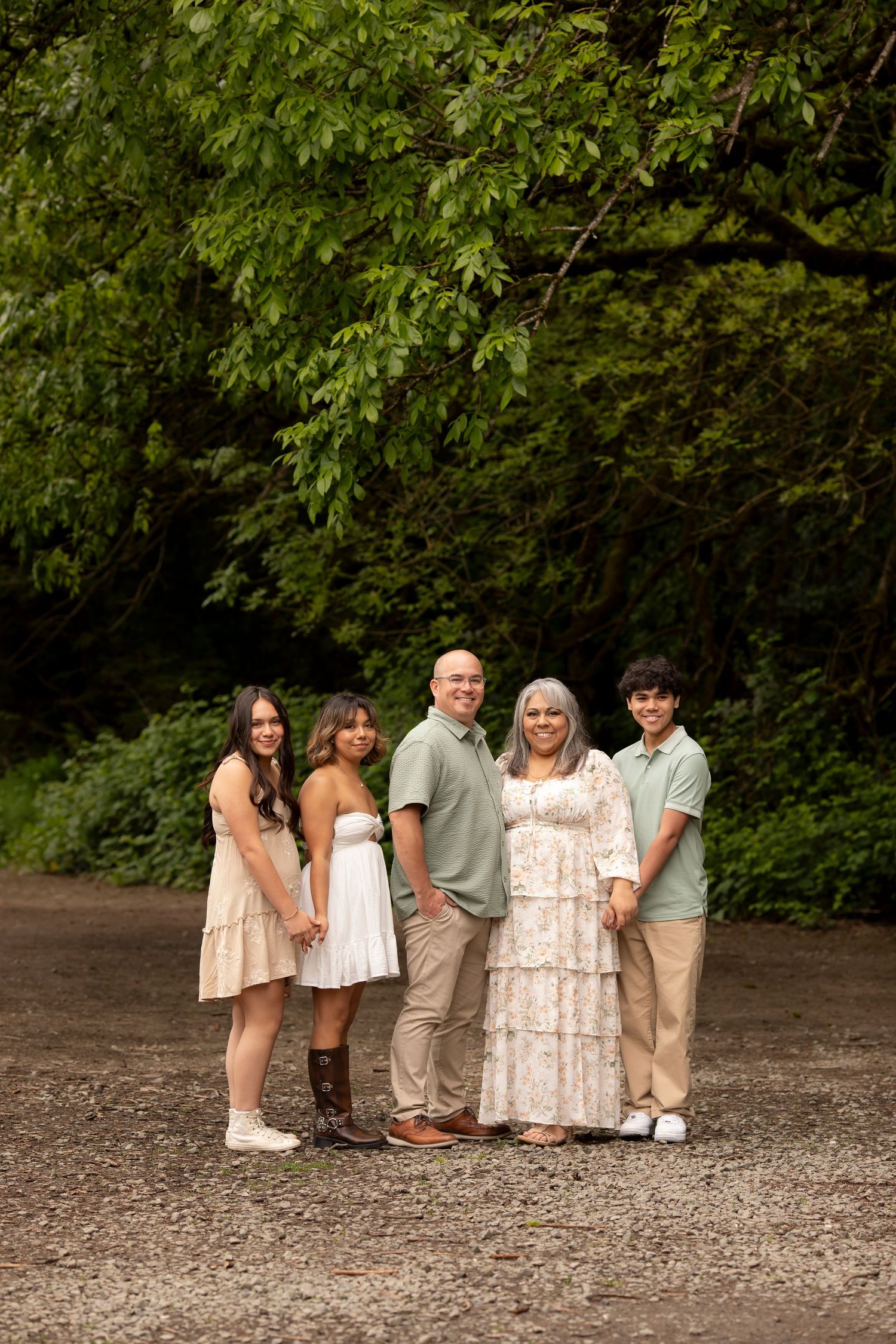 Fine art portrait of a family photographed on a path lined with lush green trees in coordinated neutral toned outfits
