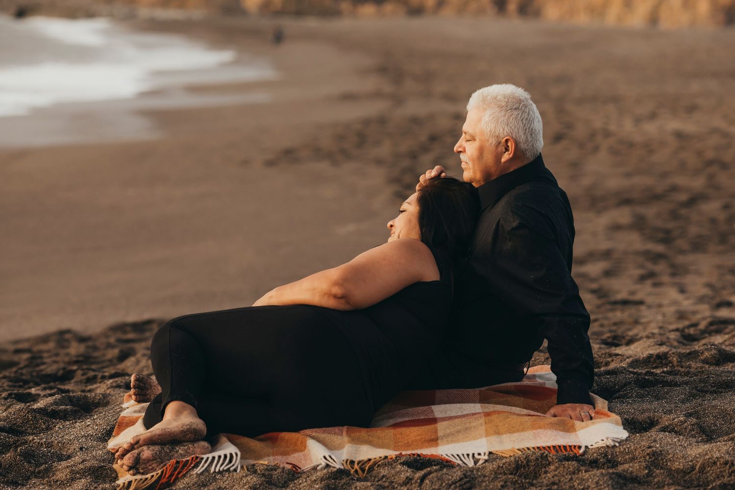 Mature couple sitting together on a beach blanket, watching the sunset during a fine art coastal portrait session in Sonoma County.