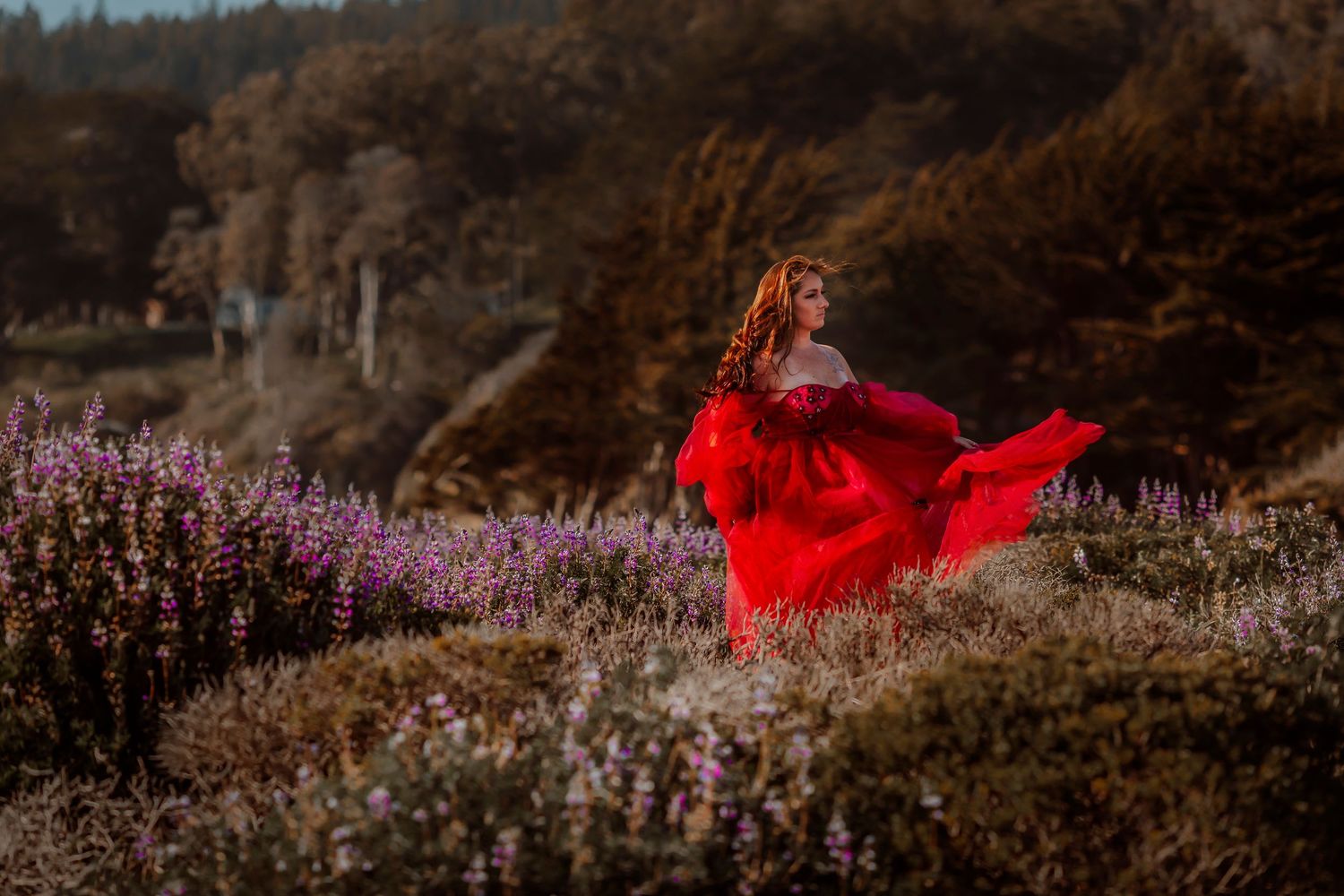 Woman in a flowing red dress standing among wildflowers in a whimsical fine art portrait, inspired by nature and storytelling.