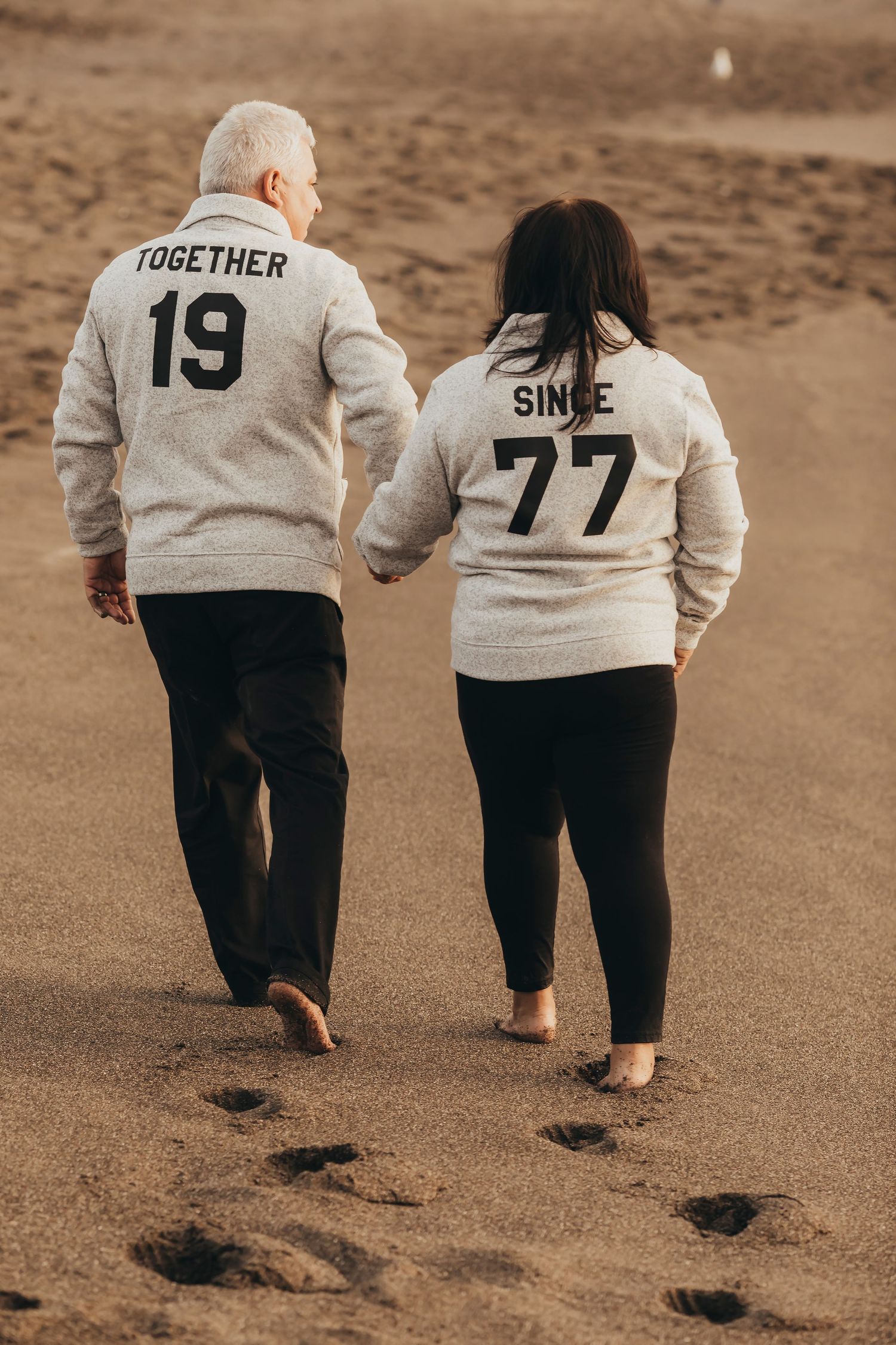Mature couple walking hand and hand on the beach wearing matching 