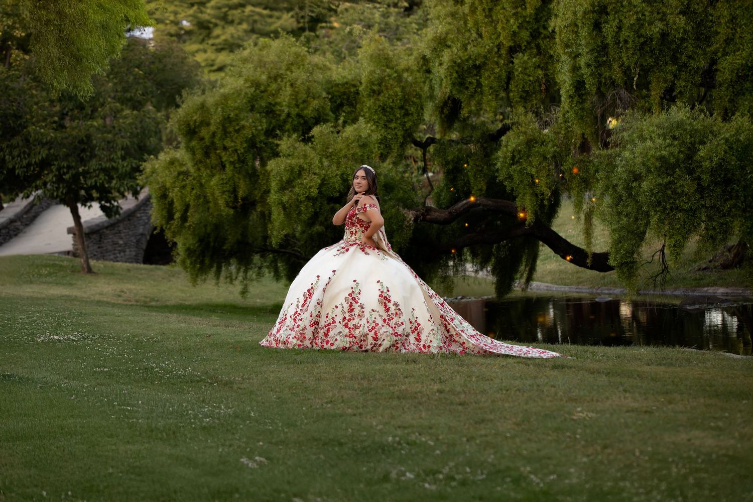 Find art quinceañera portrait featuring a young woman in an ornate floral ball gown photographed in a lush green setting