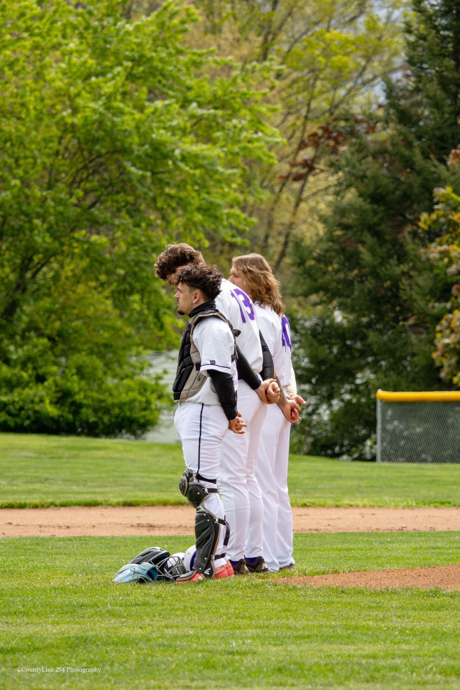 Two baseball players in white uniforms stand together on green field during a spring game.