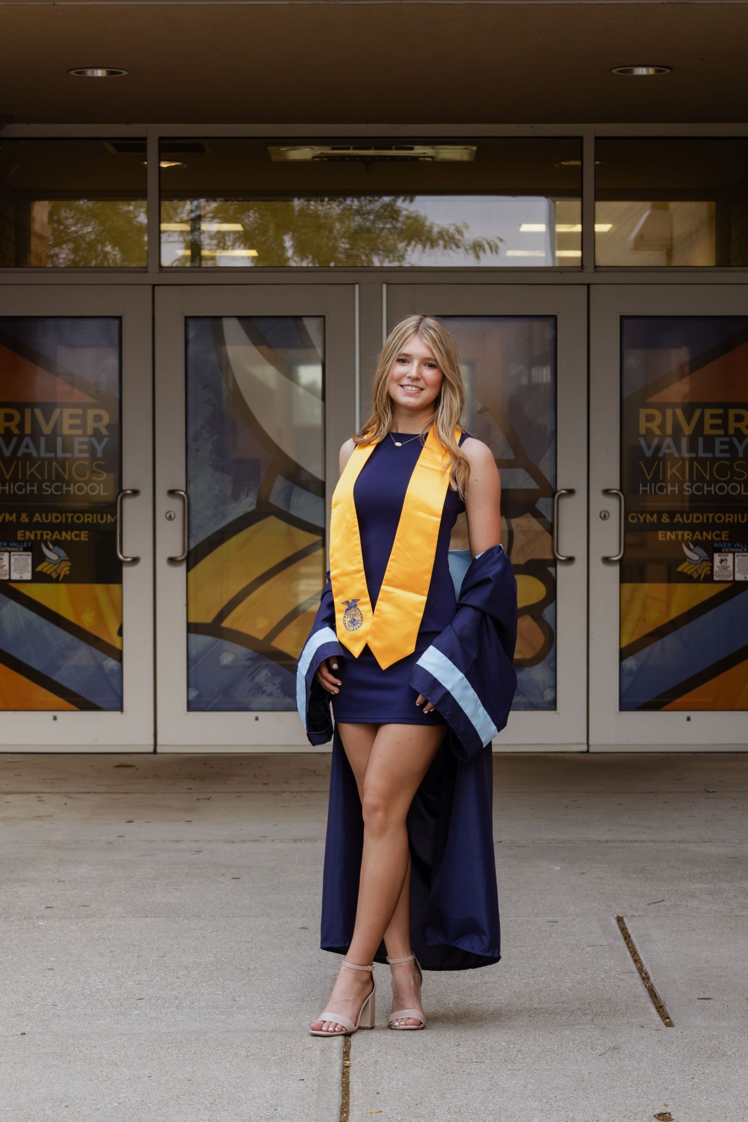 Female graduate in navy dress and gold stole standing proudly outside River Valley Vikings High School.