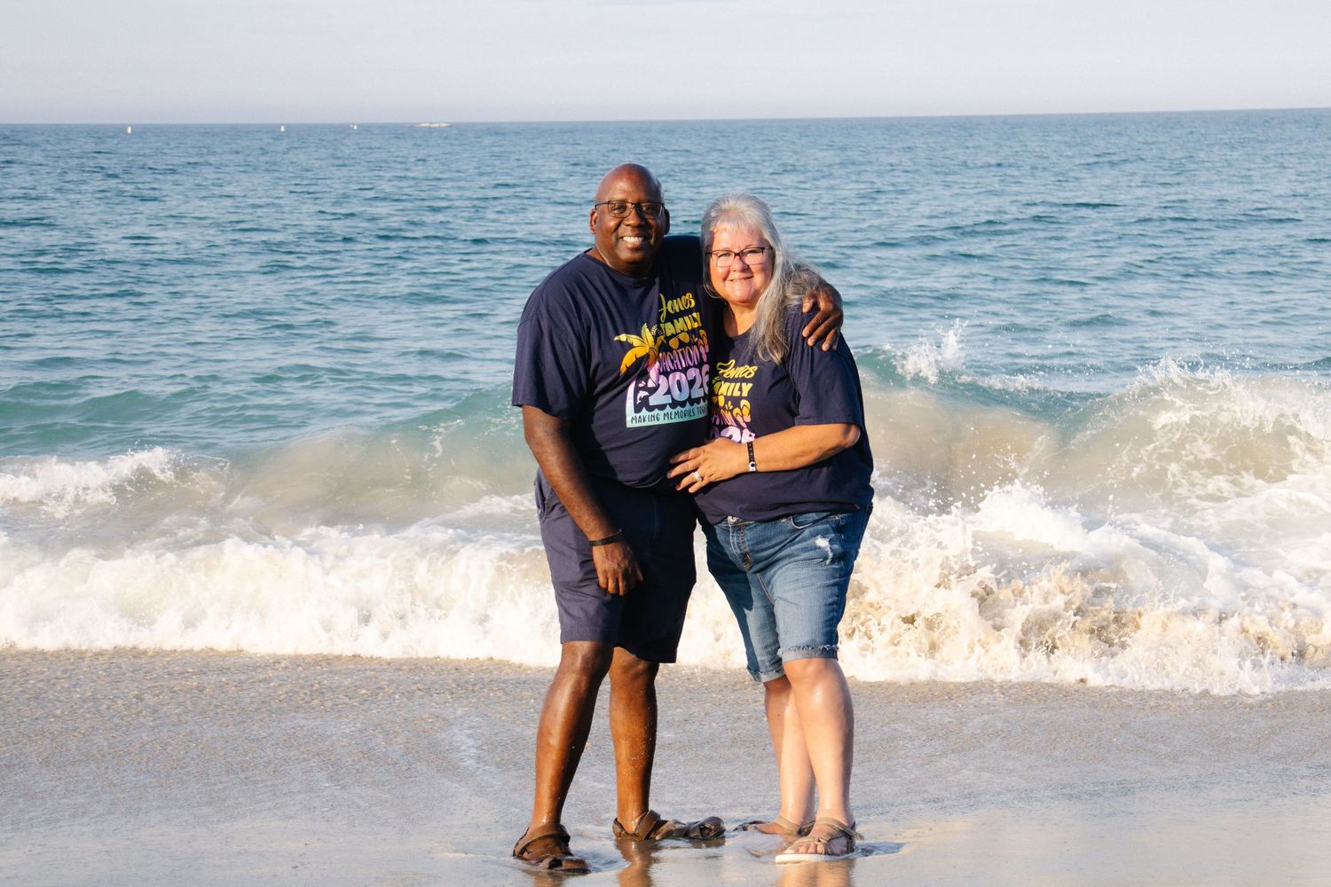 Smiling couple wearing matching navy shirts posing together on a sunny beach.