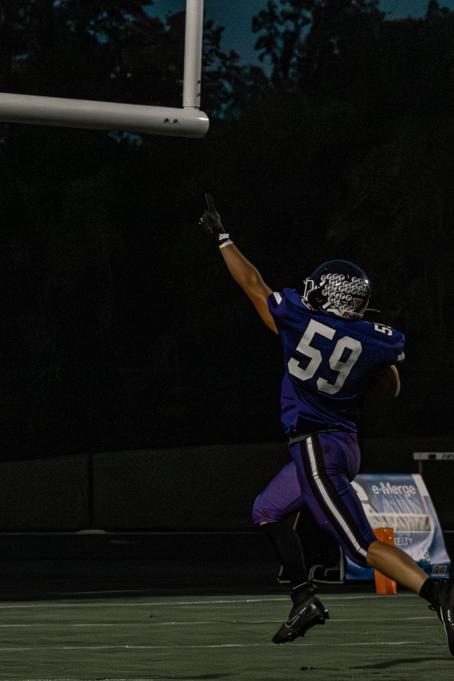 Football player number 59 in purple uniform celebrating with raised arm near goal post.